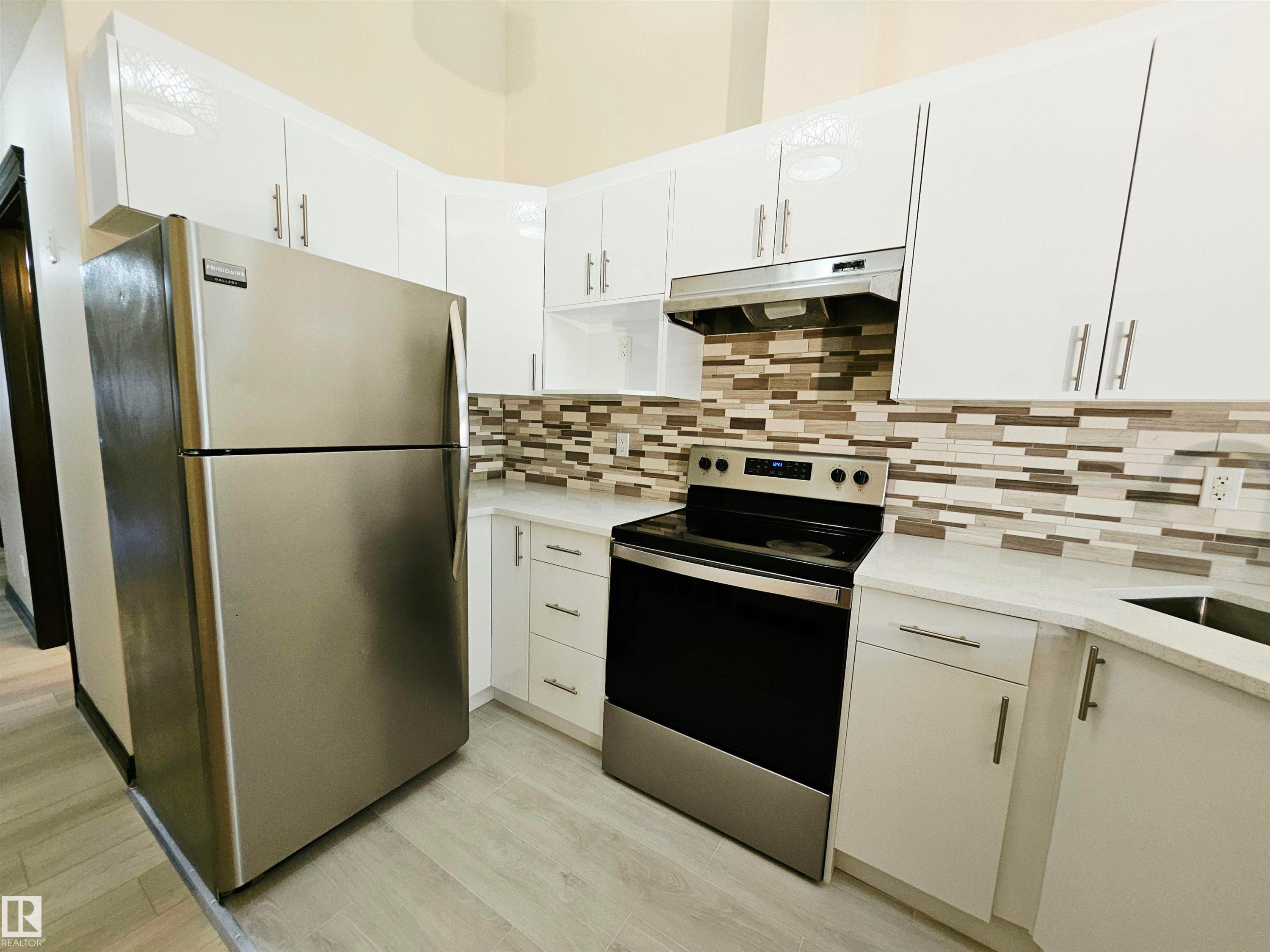 Kitchen featuring white cabinetry, light countertops, stainless steel appliances, a mosaic tile backsplash, and wood-finish flooring - 11625 88 Street Nw, Edmonton, AB