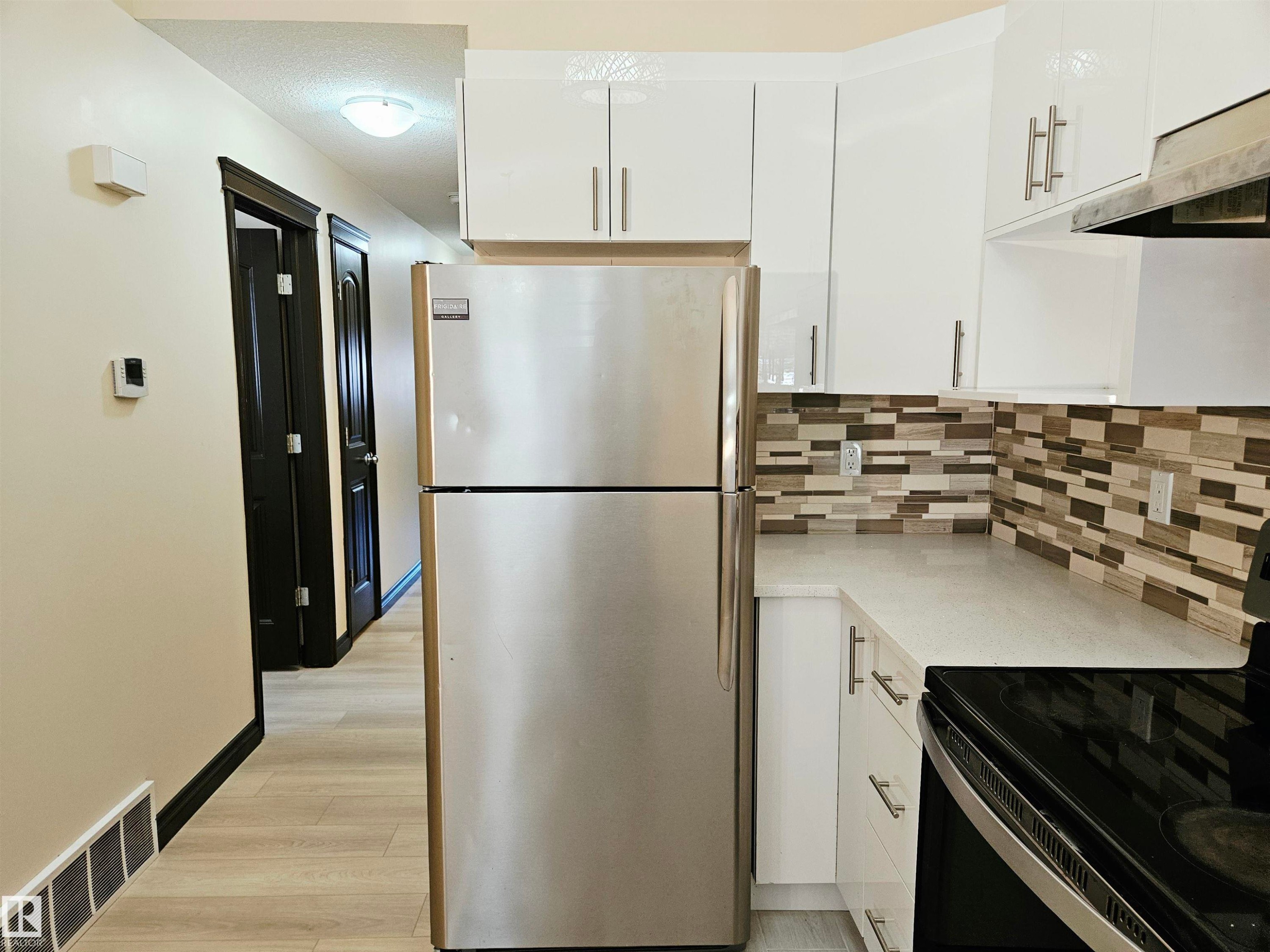 Stainless steel refrigerator, white cabinetry with silver hardware, light-toned countertop, and mosaic tile backsplash - 11625 88 Street Nw, Edmonton, AB