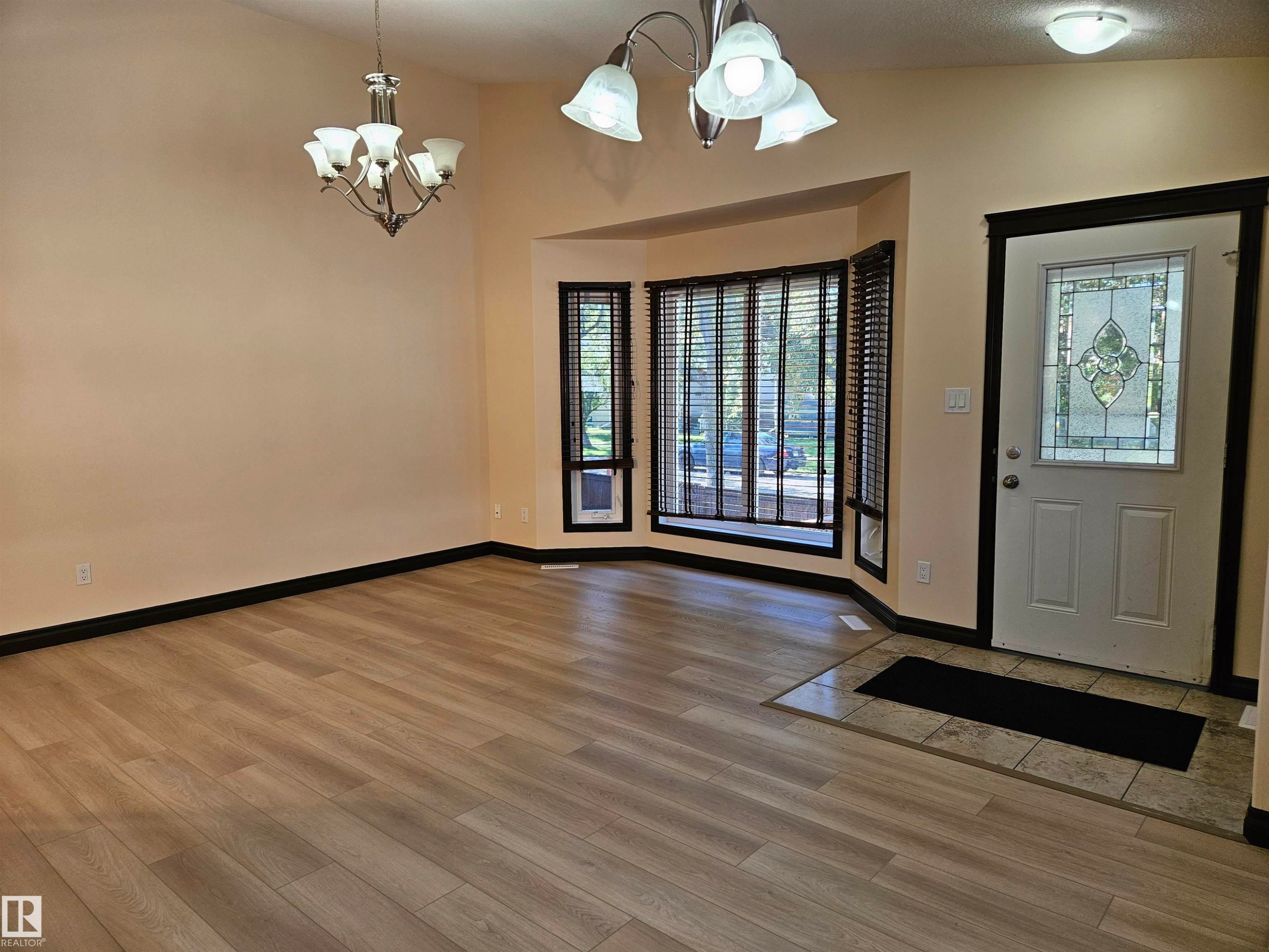 Light wood-finish flooring with tile entry, decorative glass front door, bay window, and two ceiling-mounted light fixtures - 11625 88 Street Nw, Edmonton, AB