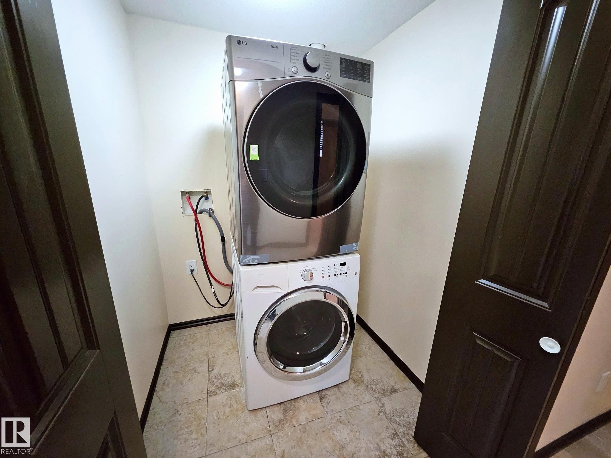 Dedicated laundry area with stacked front-load washer and dryer, tile flooring, and dark paneled doors - 11625 88 Street Nw, Edmonton, AB