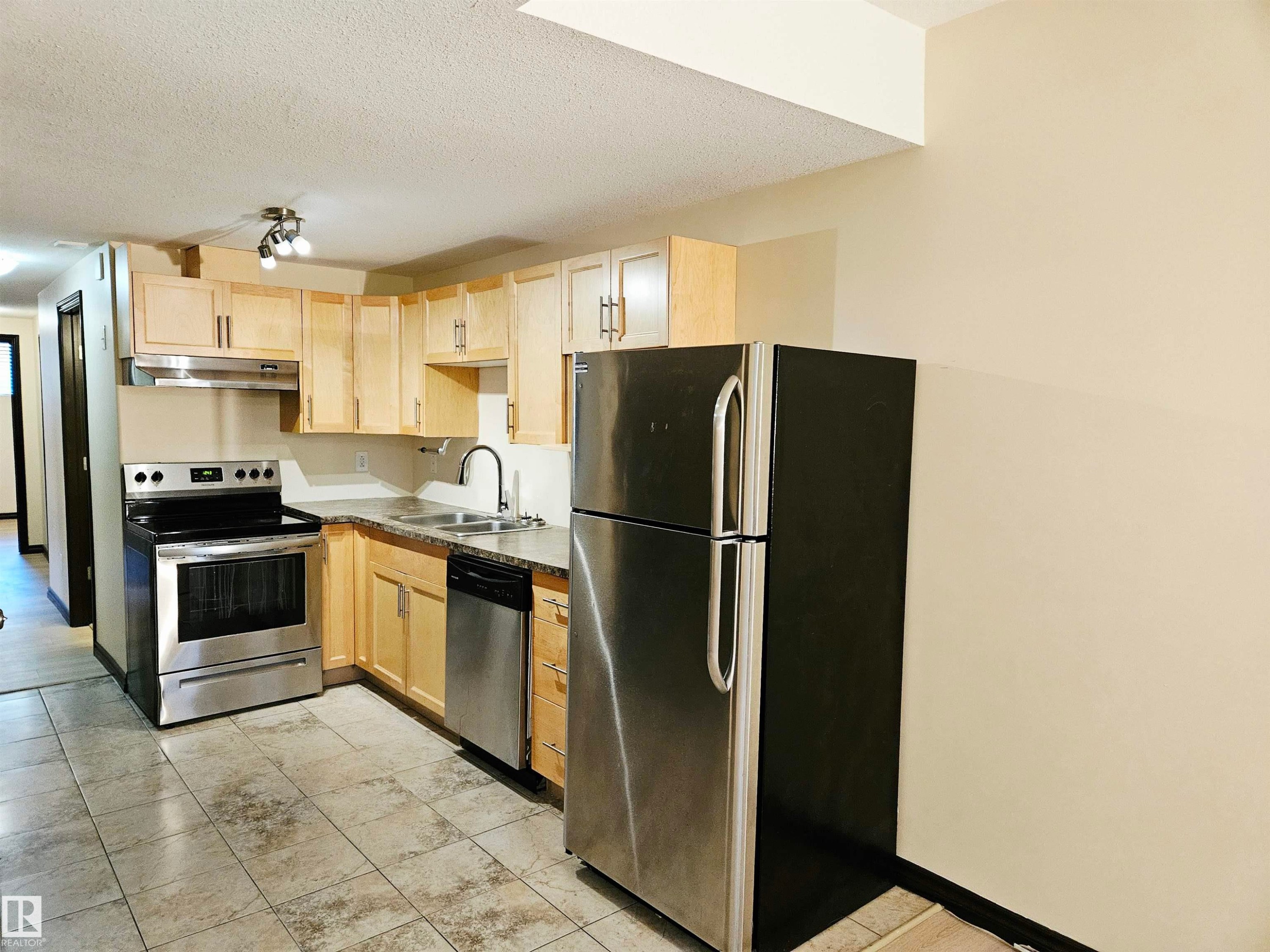 Light wood-finish cabinetry, stainless steel appliances, dark countertop, and tile flooring - 11625 88 Street Nw, Edmonton, AB