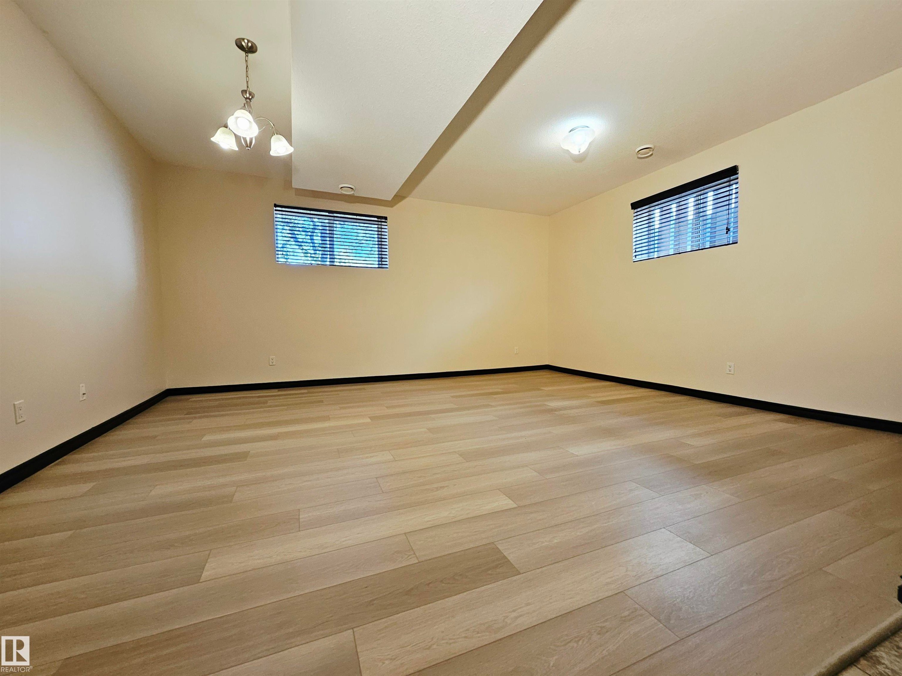 Spacious room featuring wood-finish flooring, two windows with blinds, a ceiling-mounted light fixture, and recessed lighting - 11625 88 Street Nw, Edmonton, AB