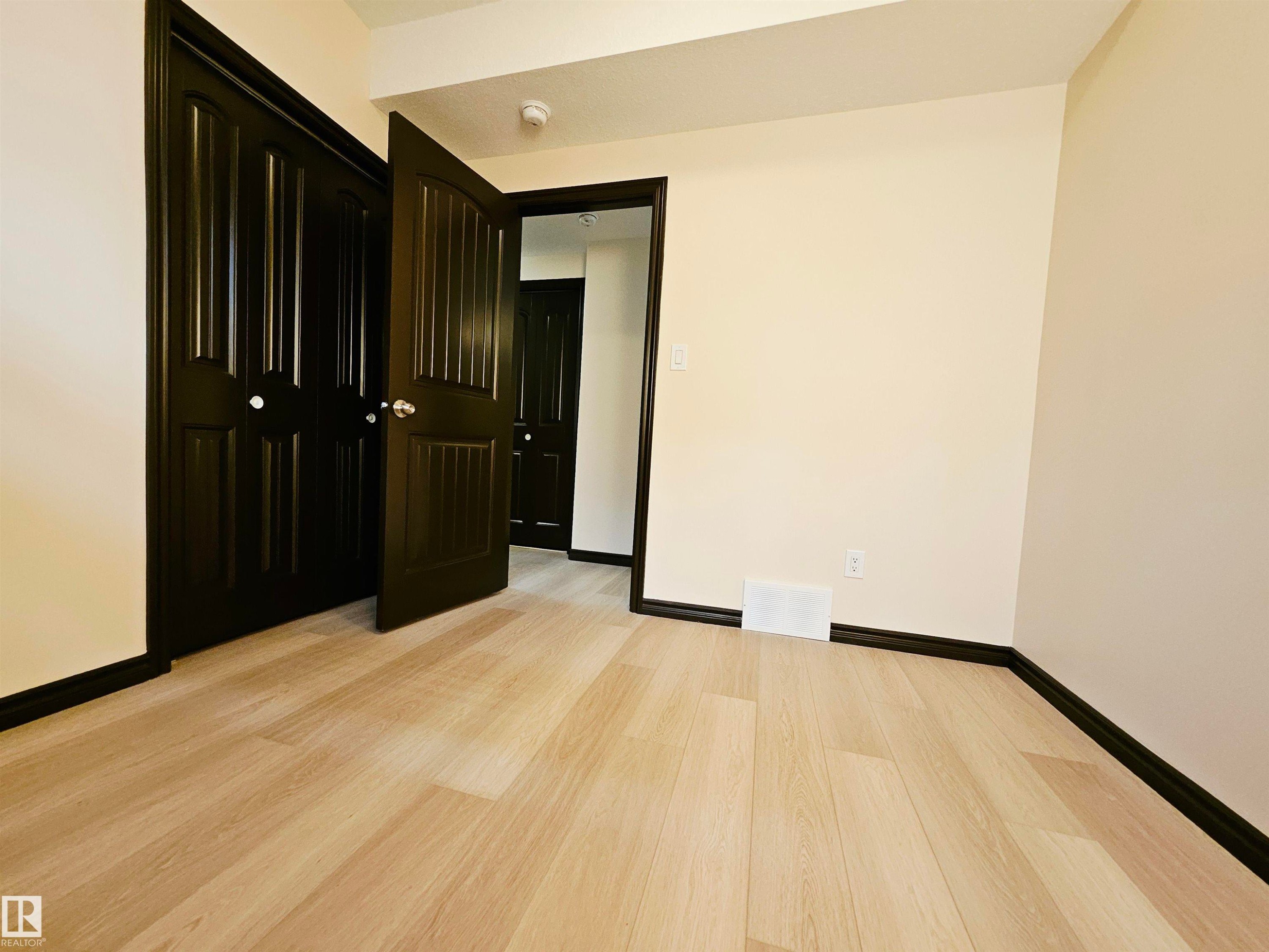 Light wood-finish flooring, dark trim, and solid dark doors - 11625 88 Street Nw, Edmonton, AB
