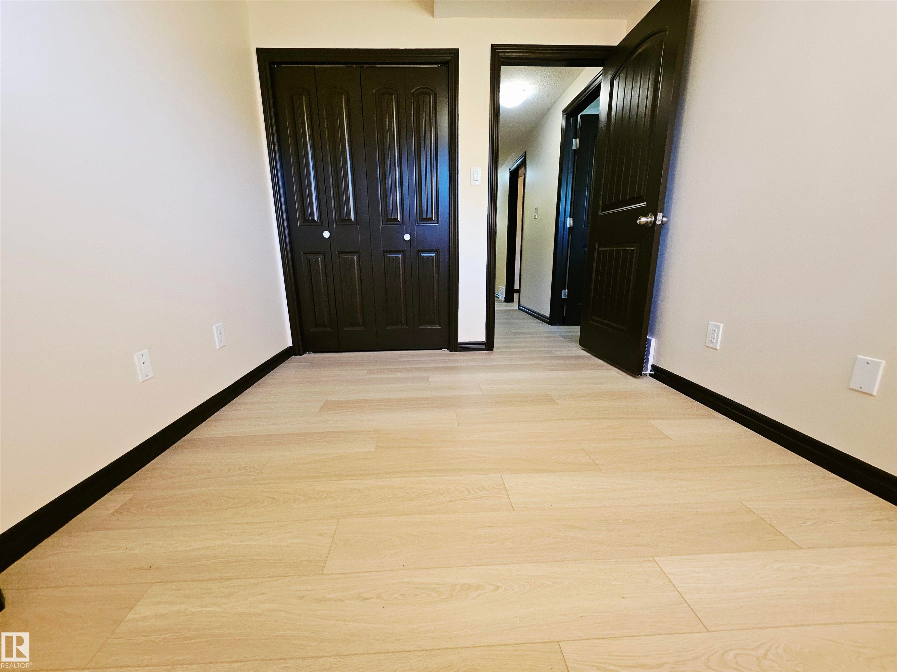 Light wood-finish flooring with dark trim, dark paneled doors, and light-colored walls - 11625 88 Street Nw, Edmonton, AB