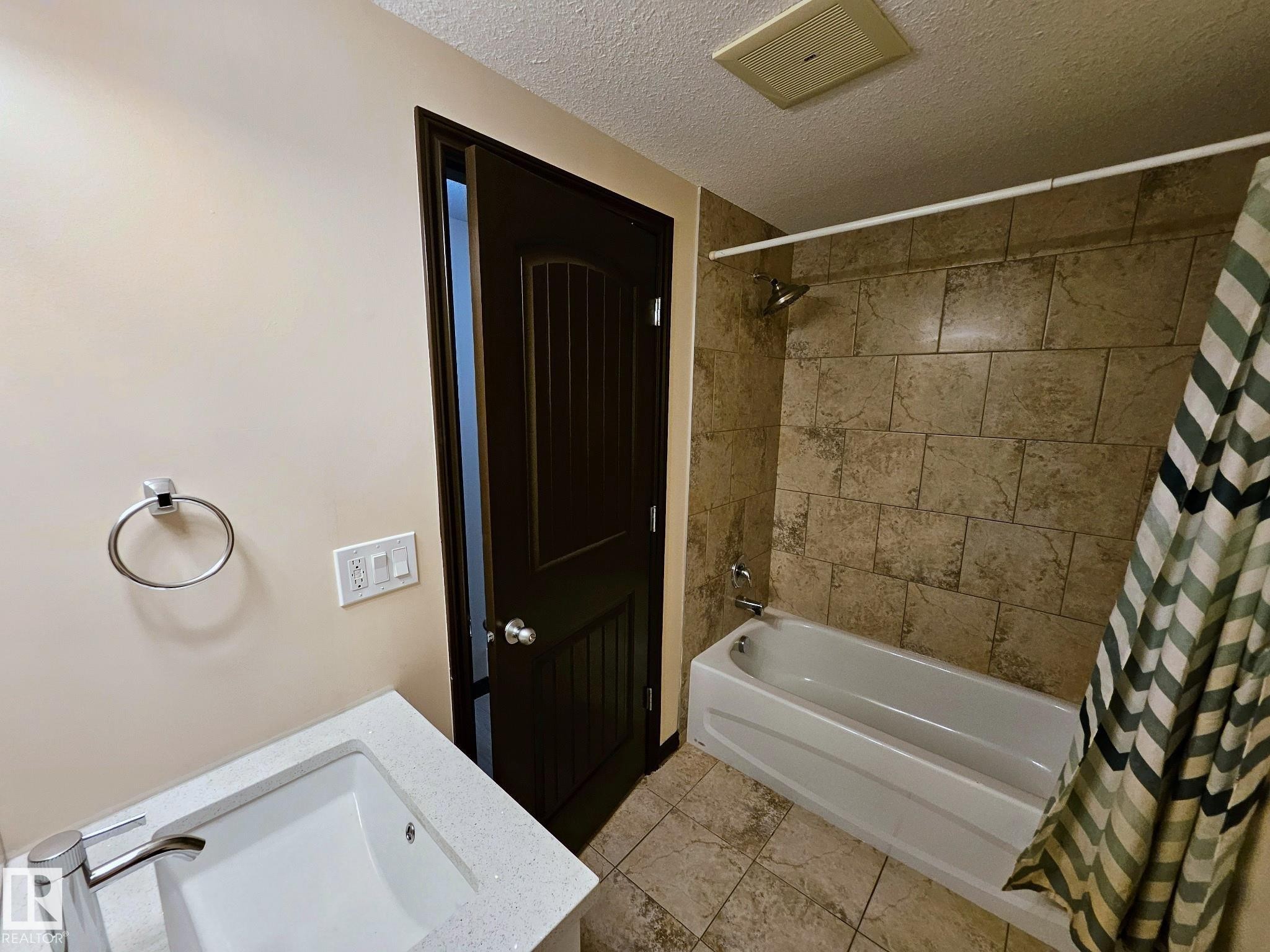 Bathtub with shower, tile surround, integrated sink with modern faucet, and dark wood-finish paneled door - 11625 88 Street Nw, Edmonton, AB