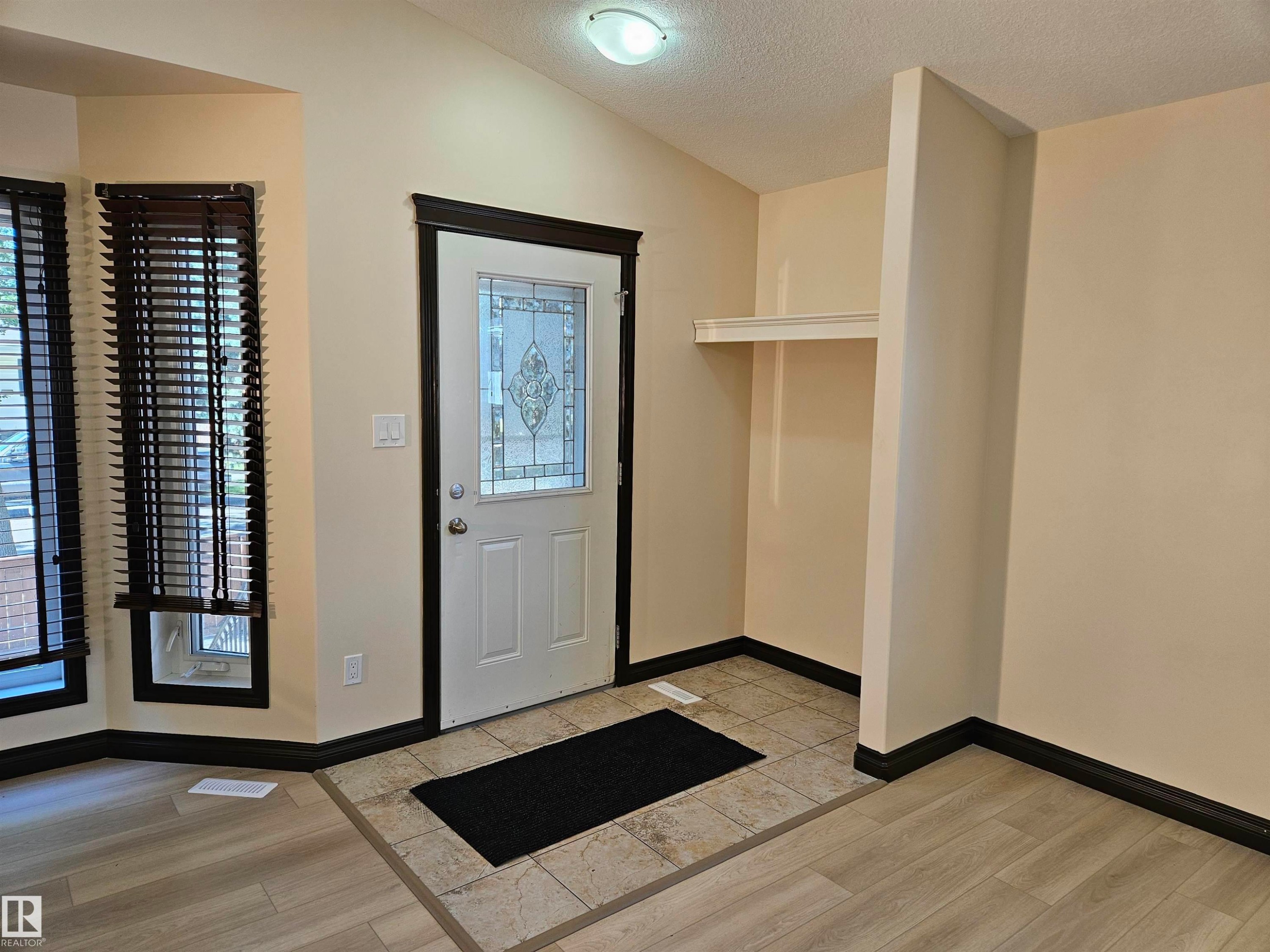 Foyer featuring a decorative glass panel entry door, vaulted ceiling, built-in shelving, and mixed flooring with tile and wood-finish planks - 11625 88 Street Nw, Edmonton, AB
