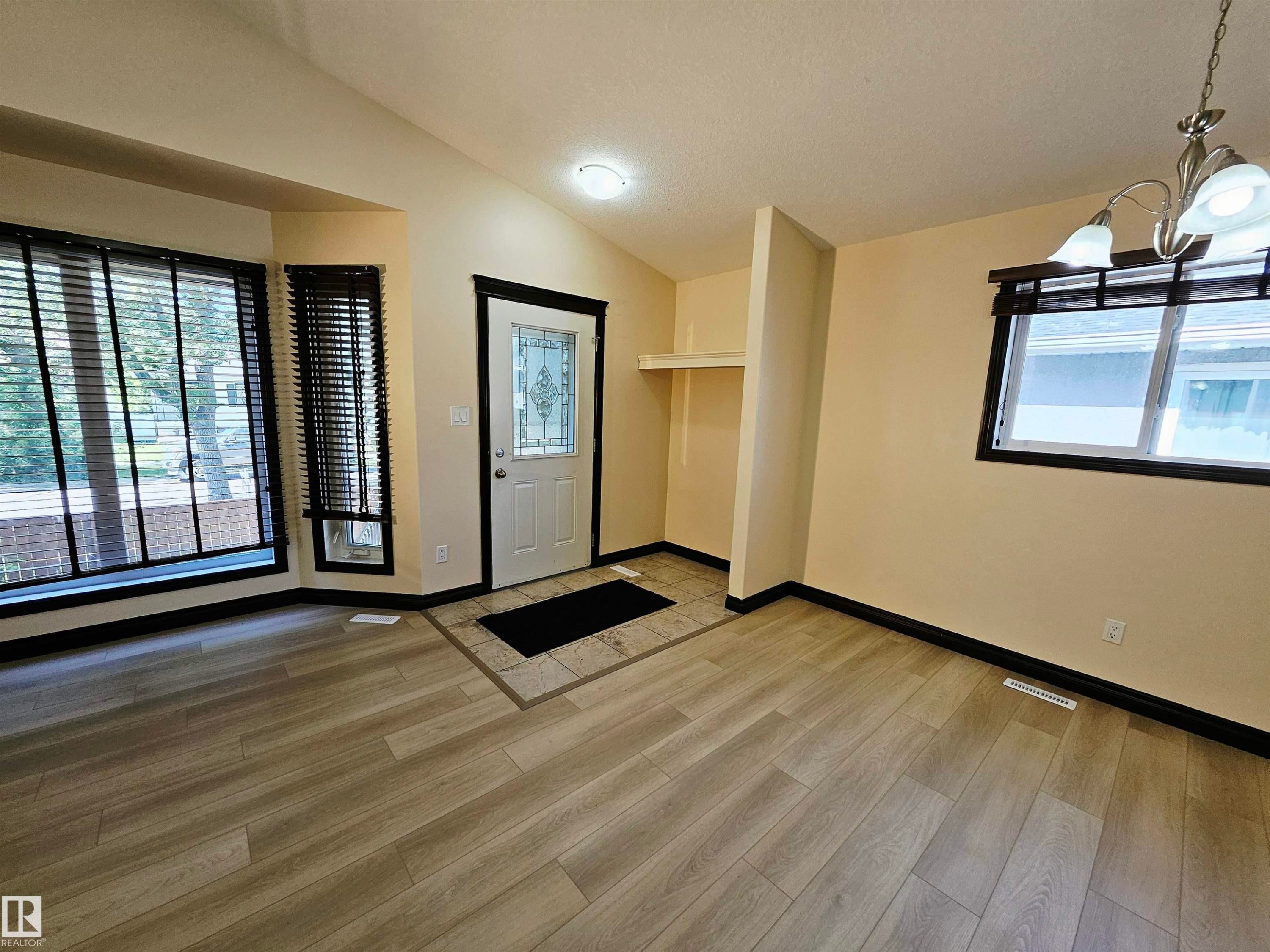 Wood-finish flooring throughout, bay window with blinds, front entry door with decorative glass inlay, recessed ceiling light, and a built-in shelving unit - 11625 88 Street Nw, Edmonton, AB