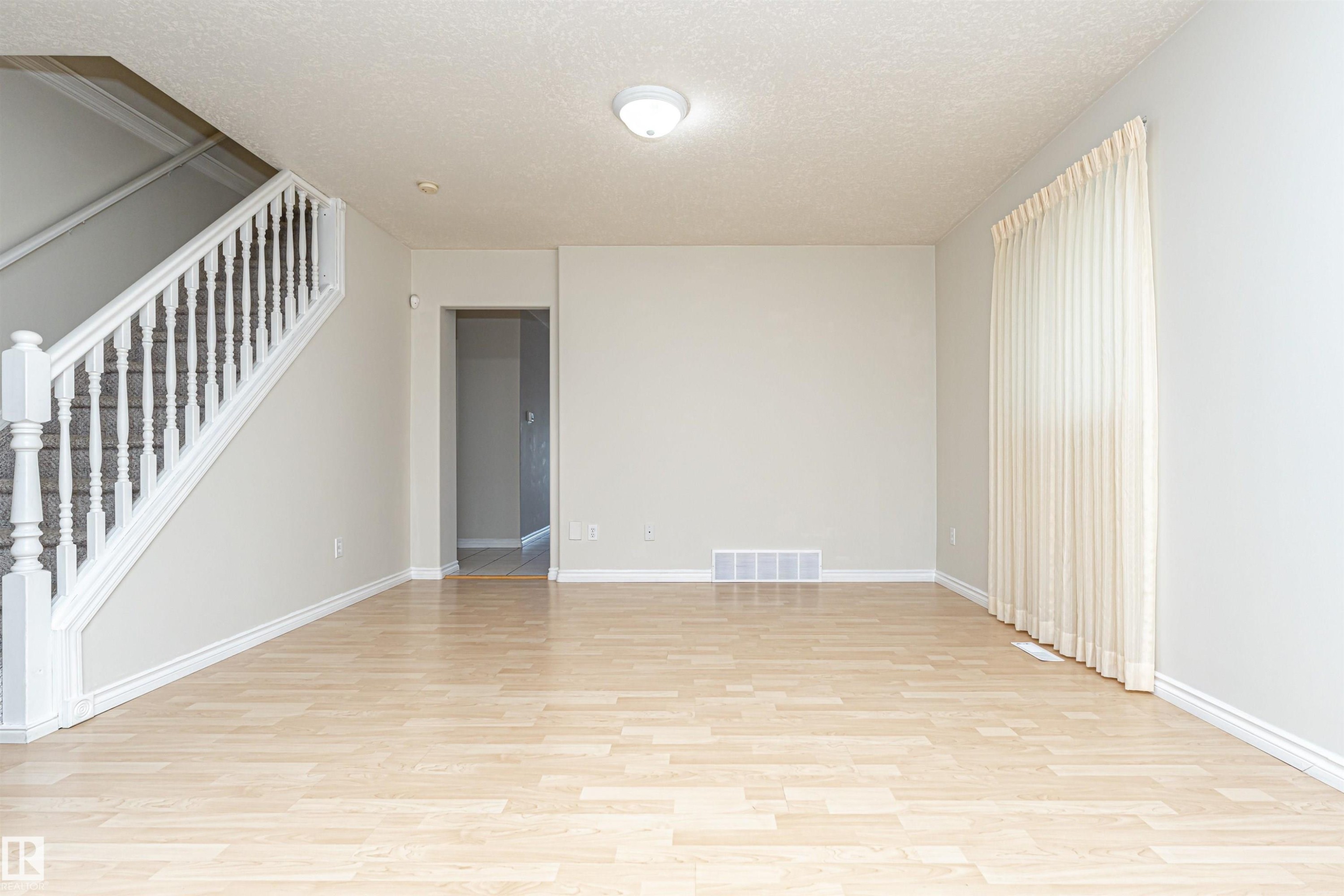 Light wood-finish flooring, staircase with white spindles, neutral wall color, and window with vertical blinds - 12241 93 Street Nw, Edmonton, AB - Indoor Photo Showing Other Room