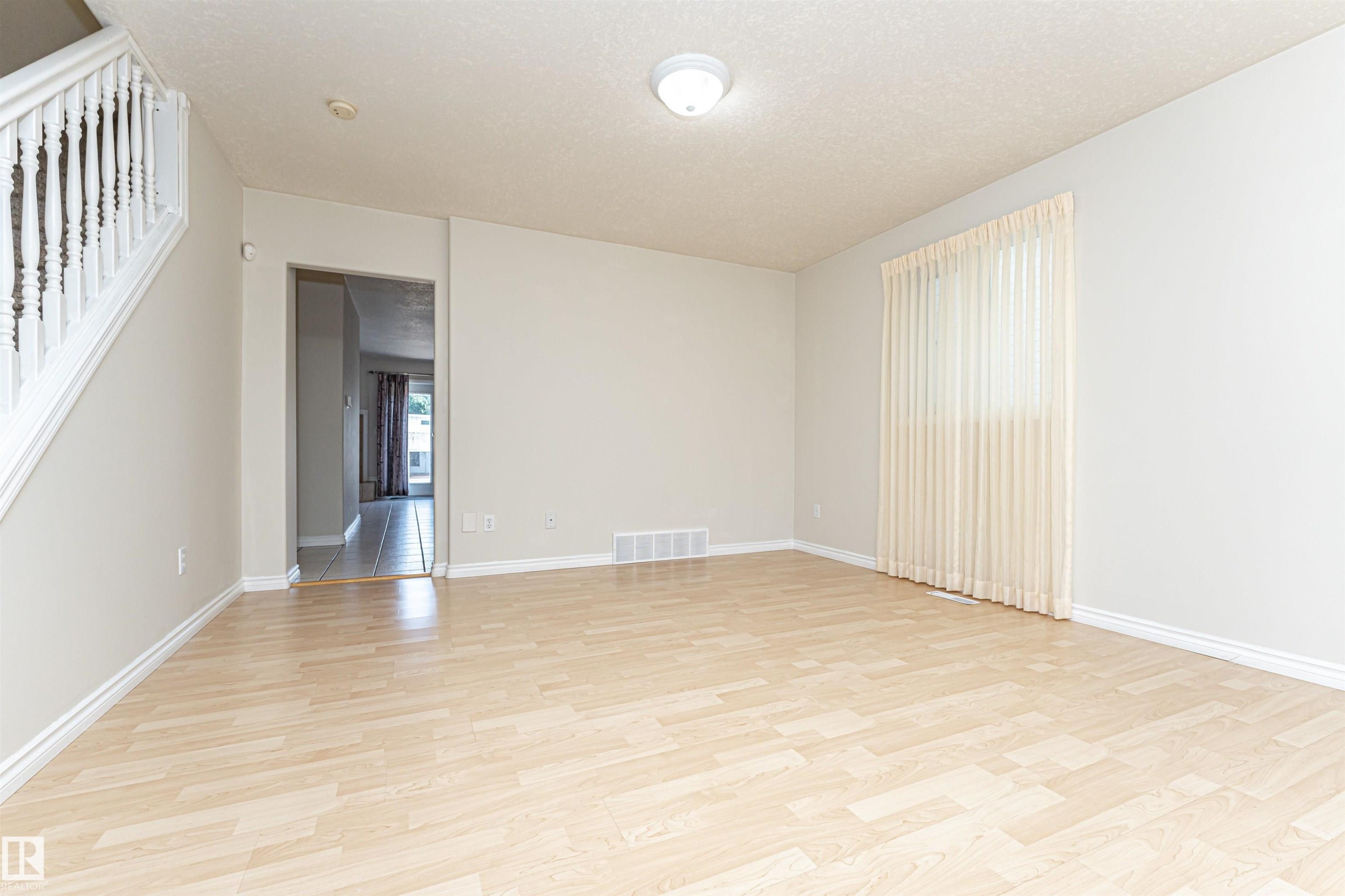 Hardwood-style flooring throughout, staircase with white balusters, light neutral wall colors, and a window with vertical blinds - 12241 93 Street Nw, Edmonton, AB - Indoor Photo Showing Other Room