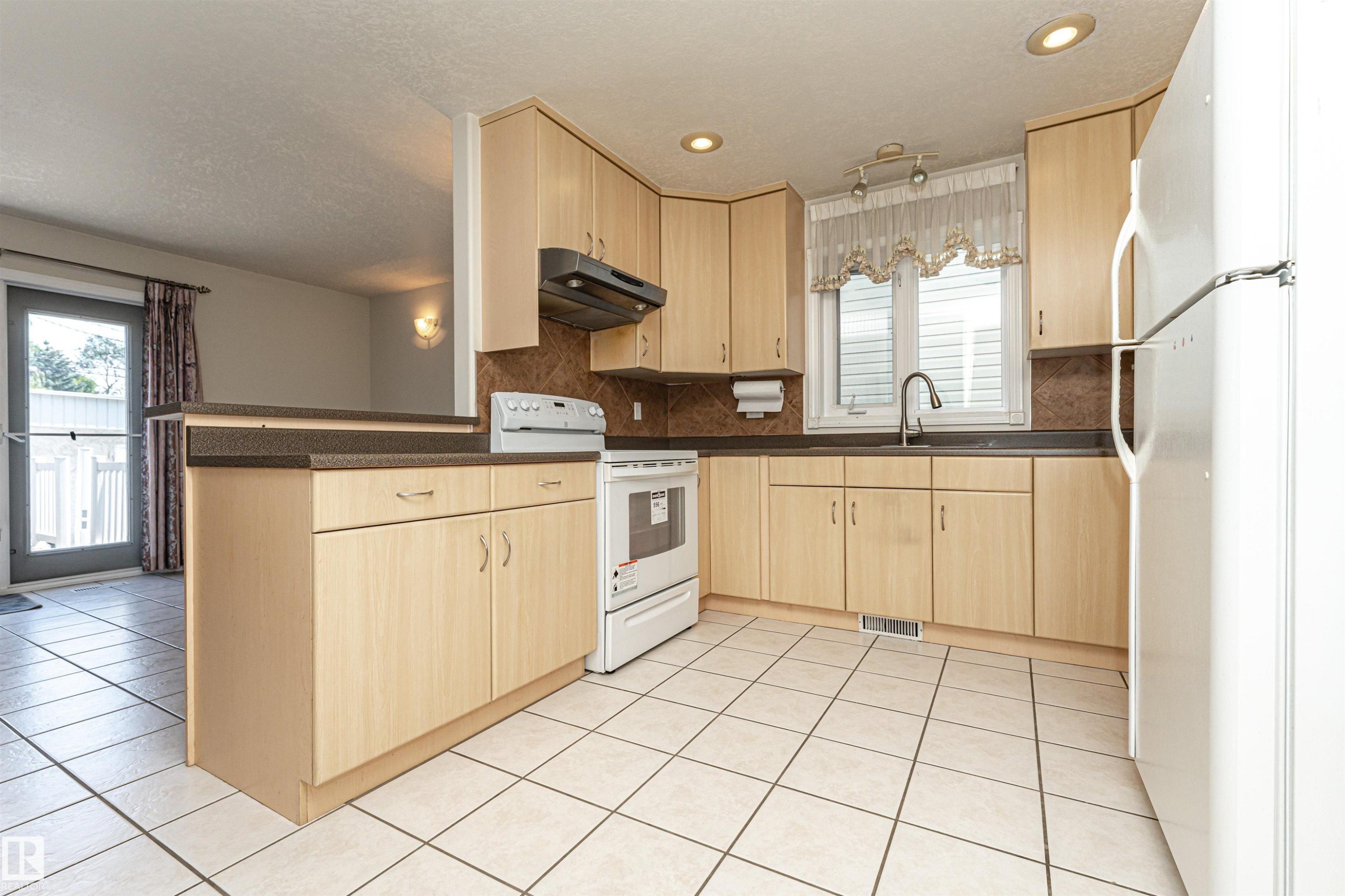 Kitchen featuring light wood-finish cabinetry, tile flooring, and integrated white appliances - 12241 93 Street Nw, Edmonton, AB - Indoor Photo Showing Kitchen