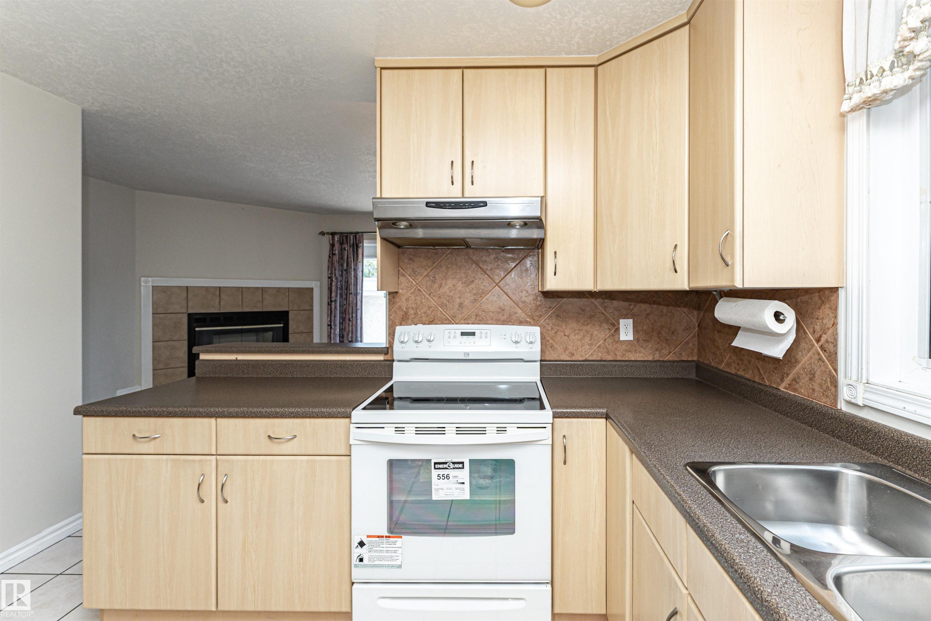 Kitchen featuring wood-finish cabinetry, dark countertops, a tile backsplash, and a stainless steel double basin sink - 12241 93 Street Nw, Edmonton, AB - Indoor Photo Showing Kitchen