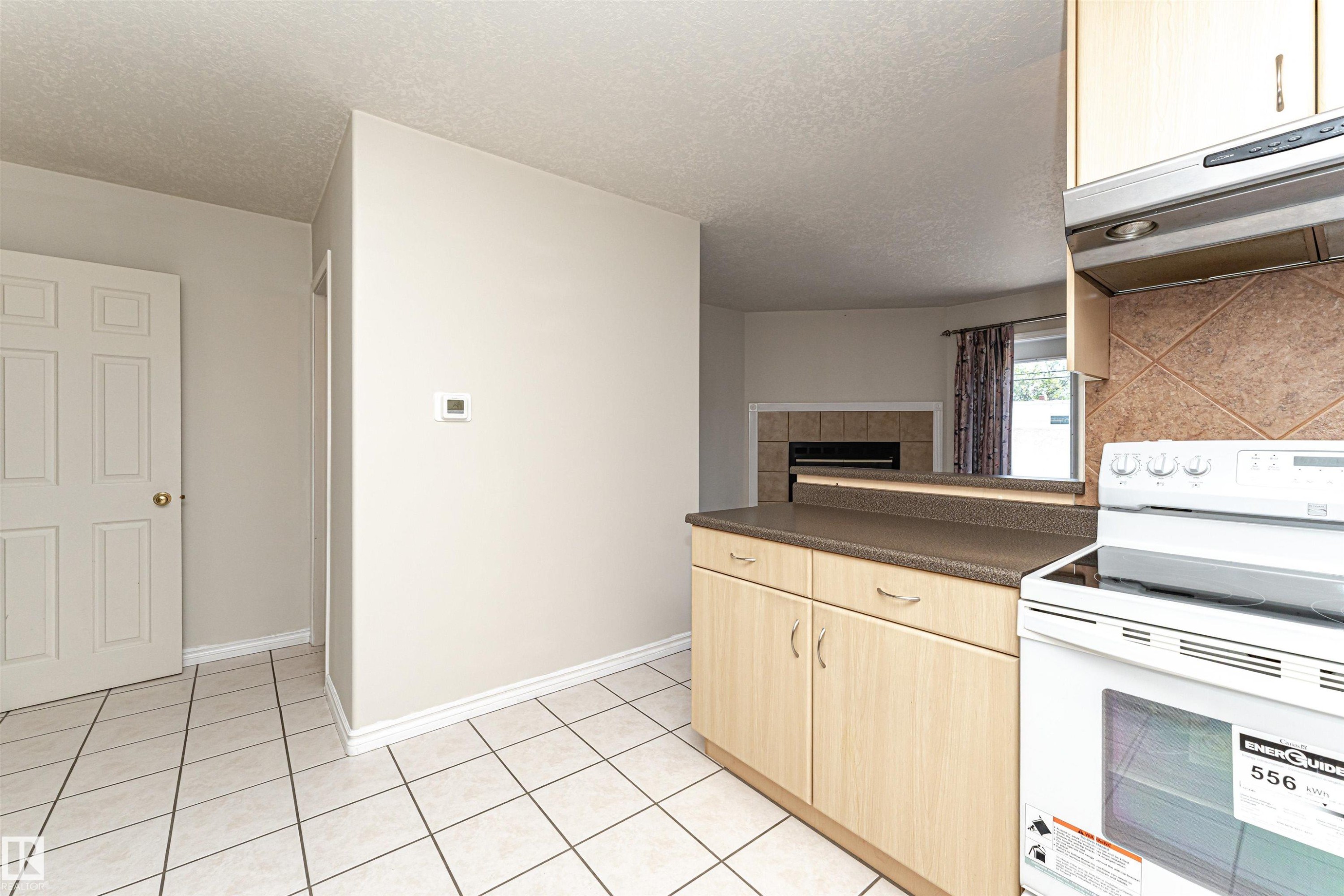 Kitchen area featuring light wood-finish cabinetry, a dark countertop, white electric range, and a tiled backsplash - 12241 93 Street Nw, Edmonton, AB - Indoor Photo Showing Kitchen