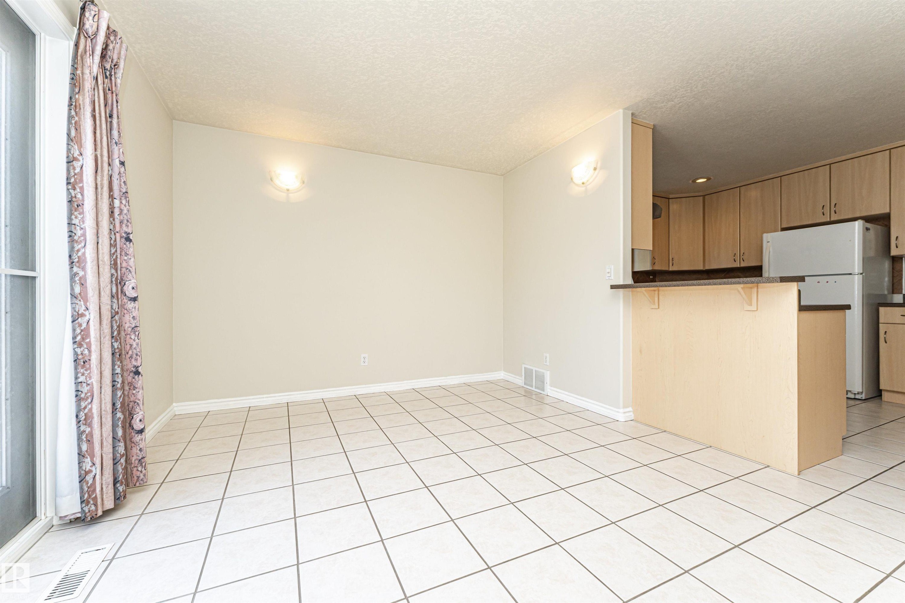 Expansive tiled flooring throughout, featuring a kitchen peninsula with a dark countertop, light wood-finish cabinetry, and integrated wall sconces - 12241 93 Street Nw, Edmonton, AB - Indoor Photo Showing Kitchen