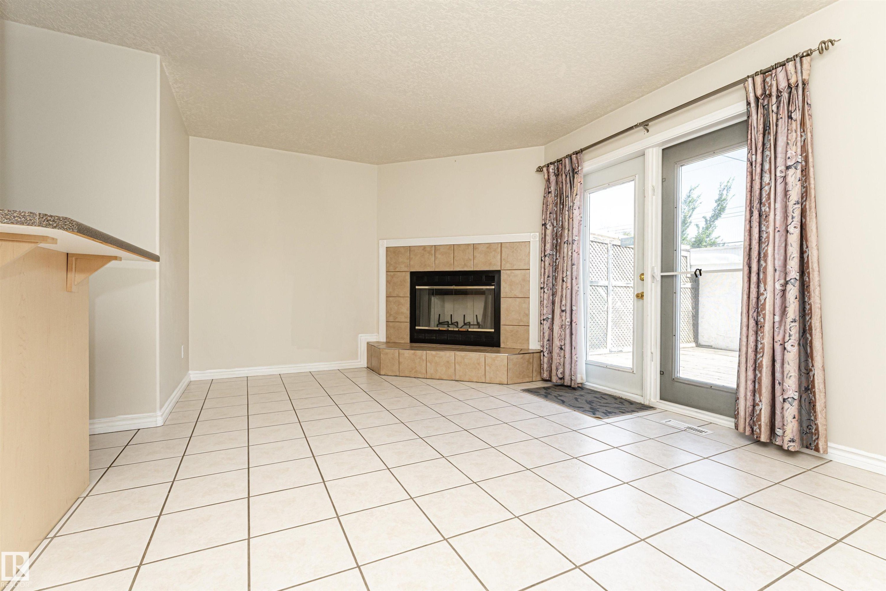 Tile flooring, corner fireplace with tile surround, sliding glass door, and breakfast bar with stone-finish countertop - 12241 93 Street Nw, Edmonton, AB - Indoor With Fireplace