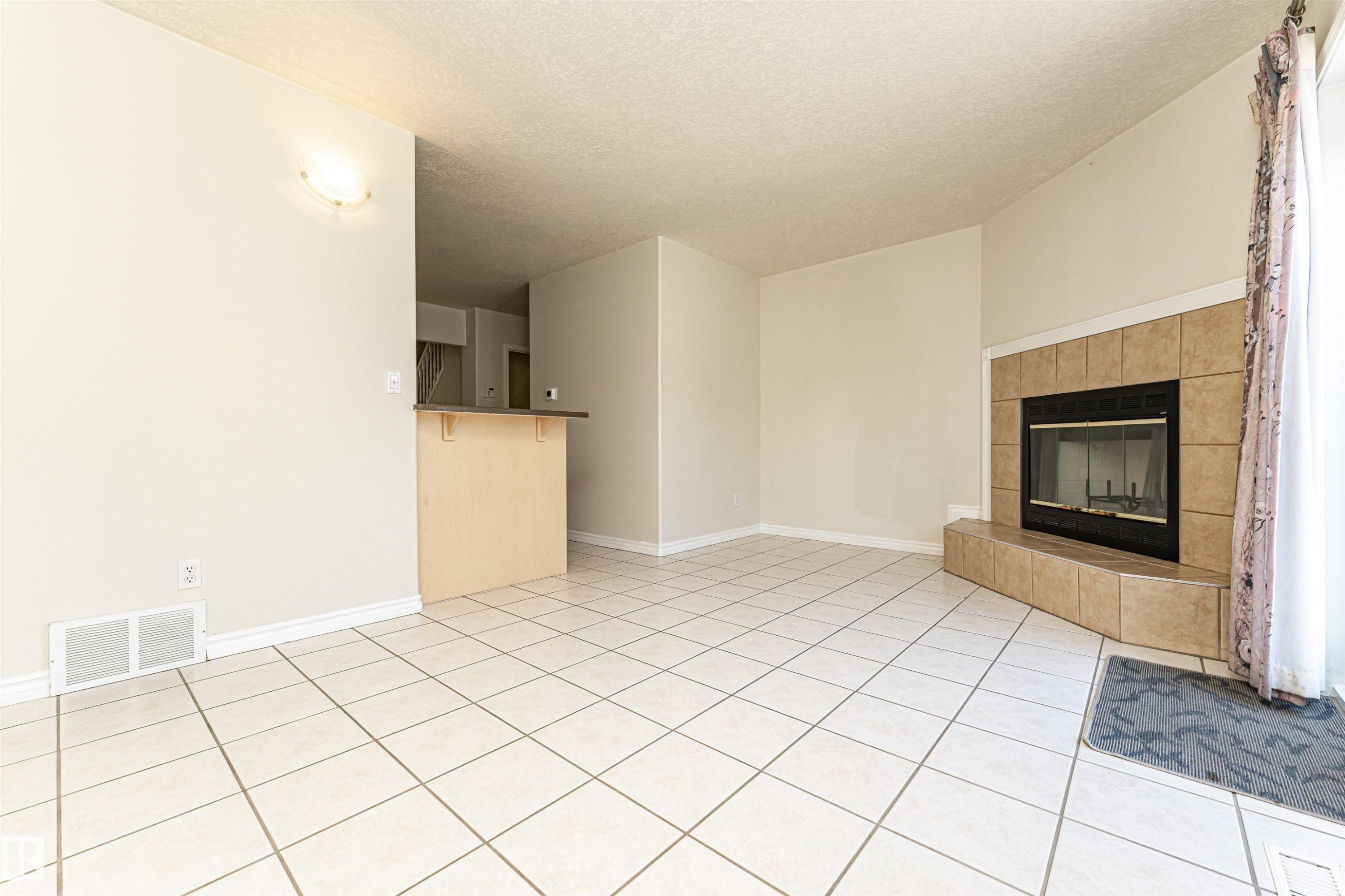 Tile flooring, corner fireplace with tile surround, built-in breakfast bar, wall sconce lighting - 12241 93 Street Nw, Edmonton, AB - Indoor With Fireplace