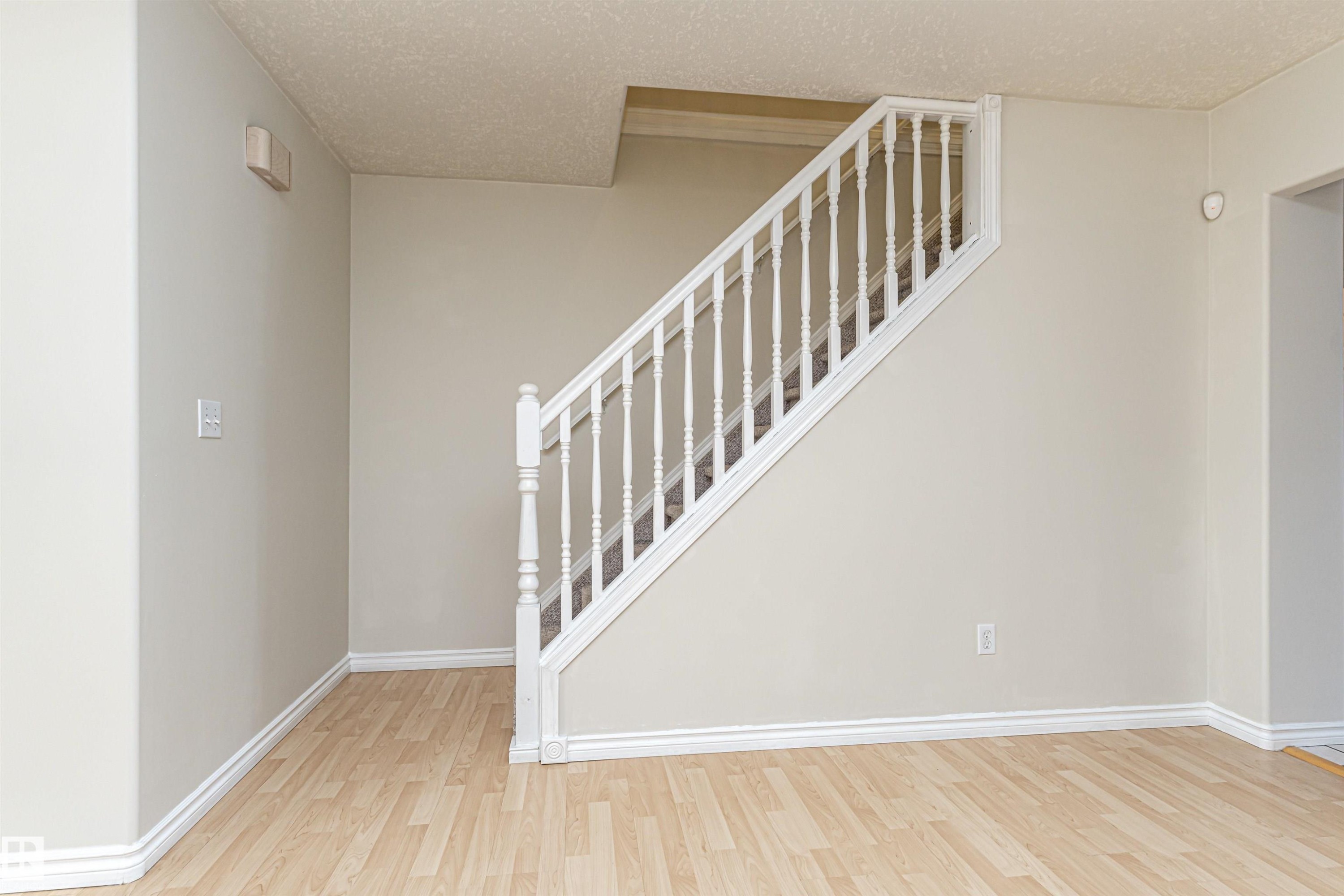 Staircase with white wood balusters and handrail, neutral painted walls, light wood-finish flooring, and white trim - 12241 93 Street Nw, Edmonton, AB - Indoor Photo Showing Other Room