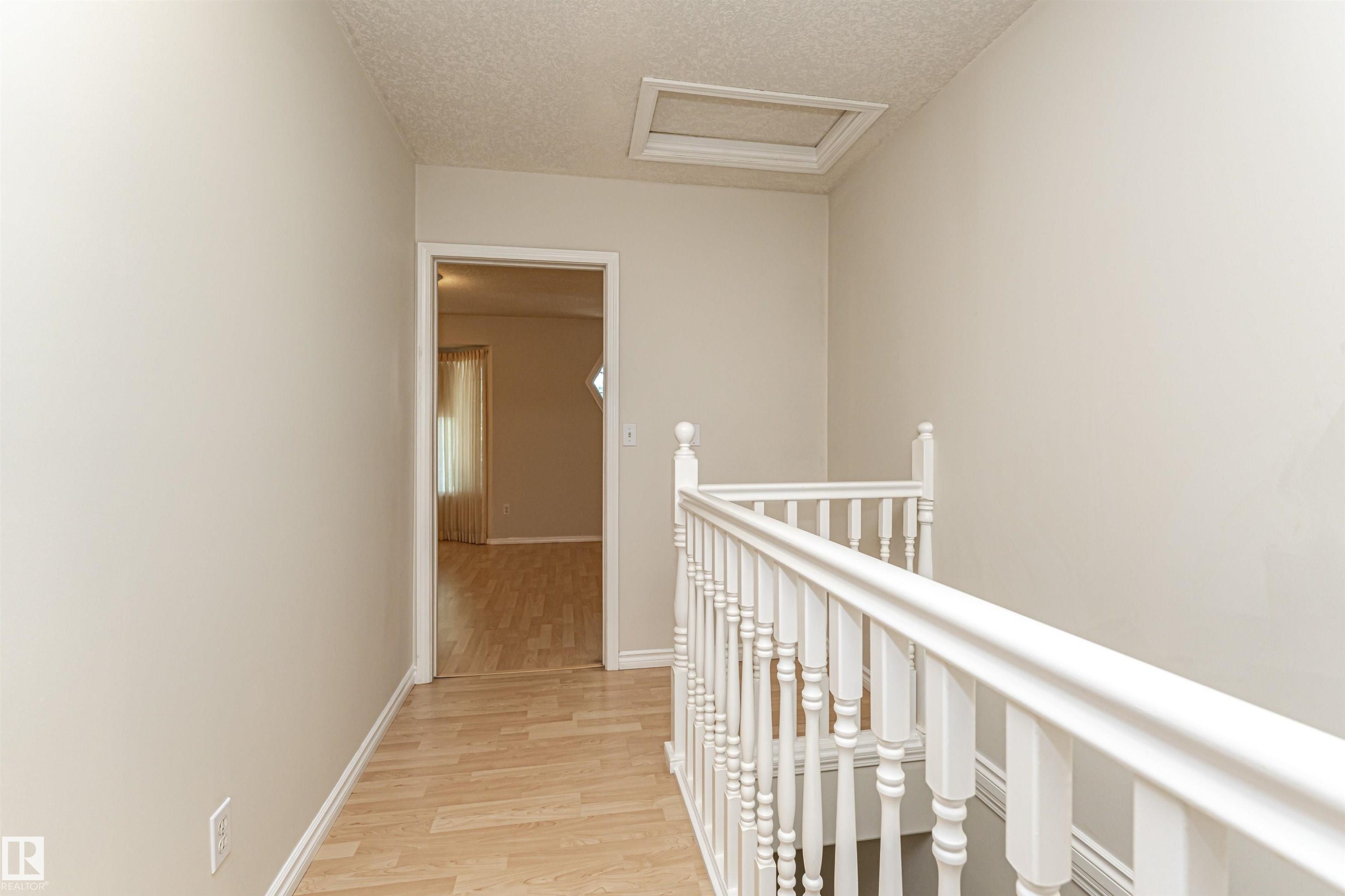 Neutral wall finishes, wood-finish flooring, white painted railing, and an attic access panel - 12241 93 Street Nw, Edmonton, AB - Indoor Photo Showing Other Room