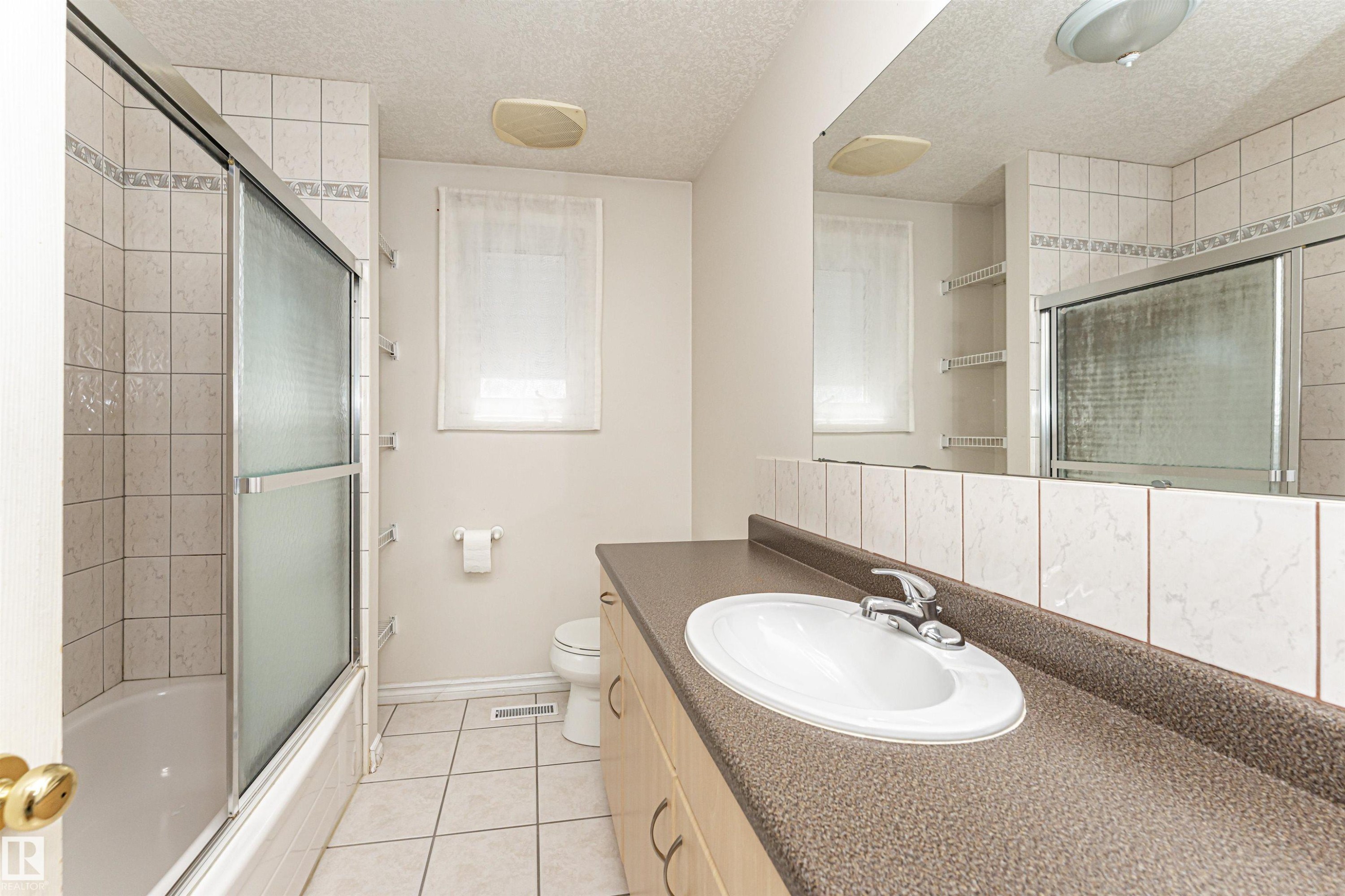 Tub and shower combination with sliding glass enclosure, white tile surround, and tile flooring - 12241 93 Street Nw, Edmonton, AB - Indoor Photo Showing Bathroom
