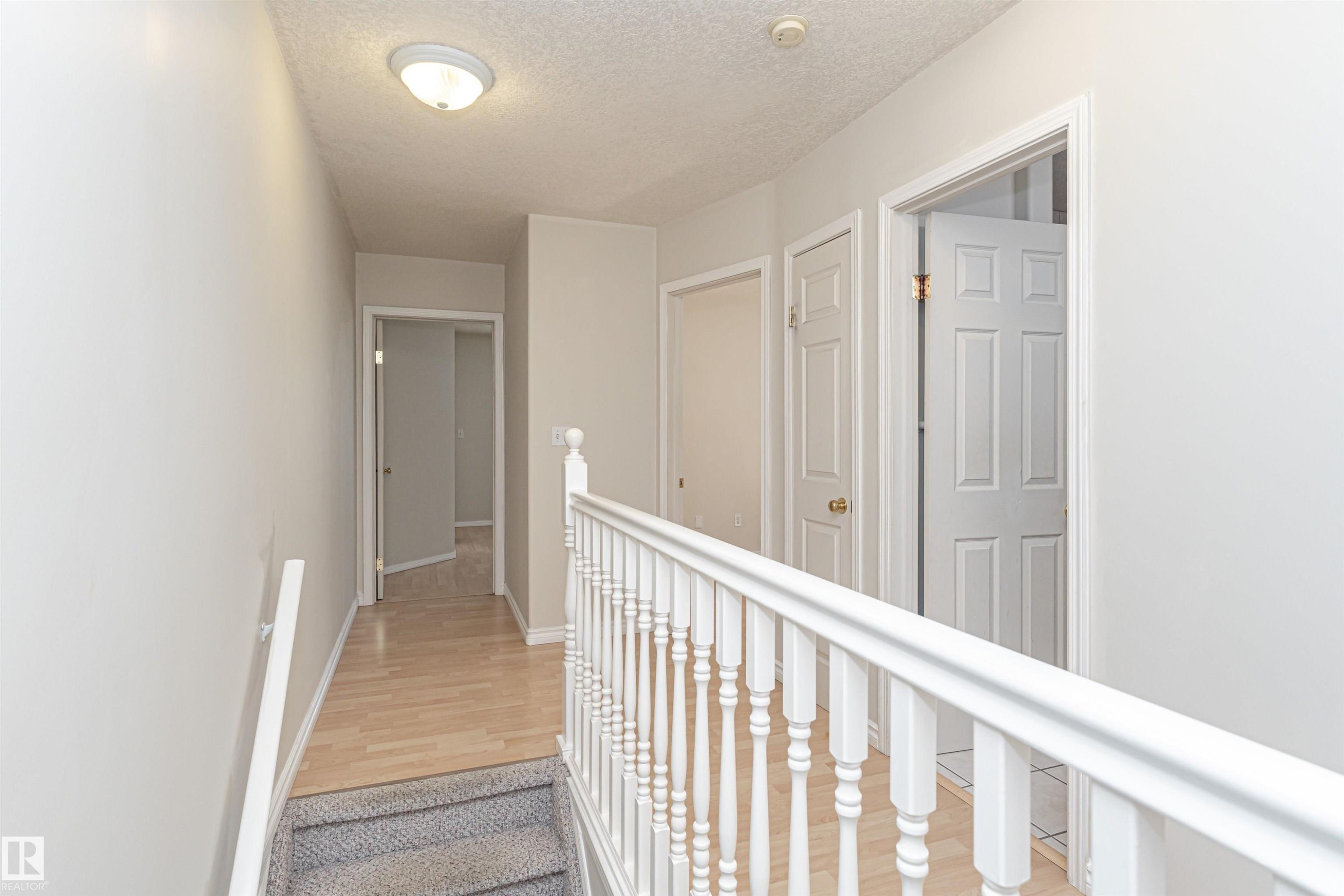 Hallway featuring wood-finish flooring, white paneled doors, and a white baluster railing - 12241 93 Street Nw, Edmonton, AB - Indoor Photo Showing Other Room