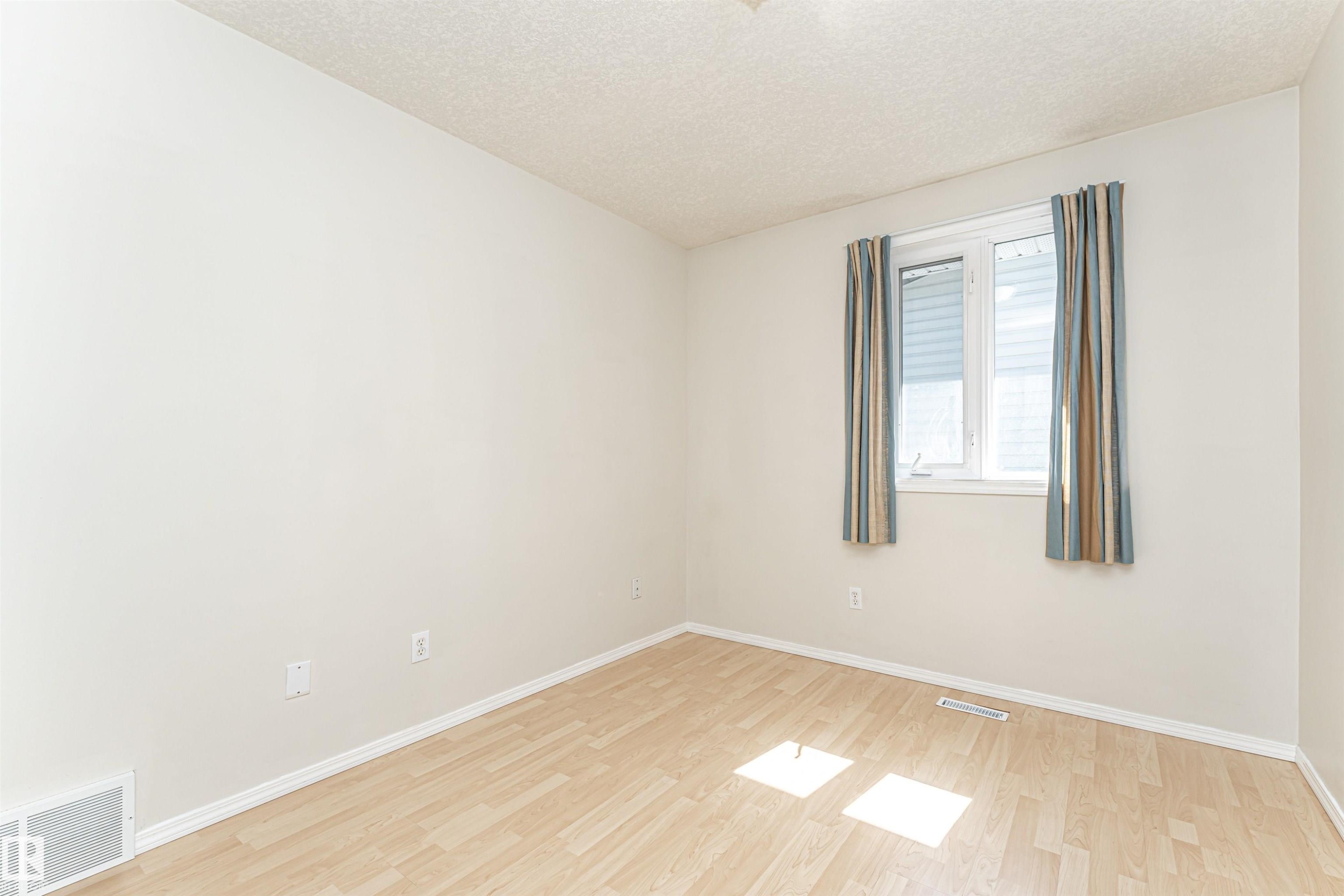 Light wood-finish flooring with white baseboards, a white window frame, and a textured white ceiling - 12241 93 Street Nw, Edmonton, AB - Indoor Photo Showing Other Room