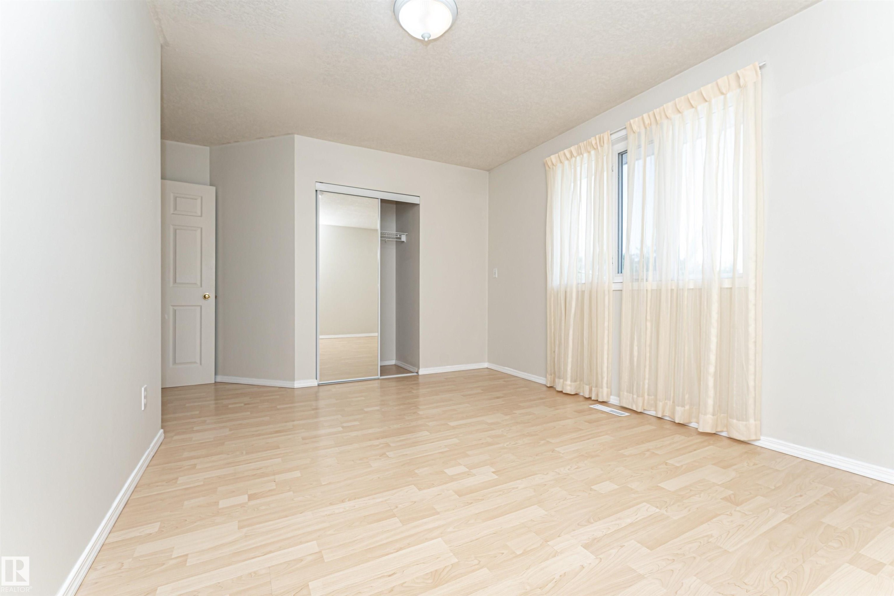 Light wood-finish flooring, a window with sheer curtains, a mirrored closet, and a white ceiling light fixture - 12241 93 Street Nw, Edmonton, AB - Indoor Photo Showing Other Room