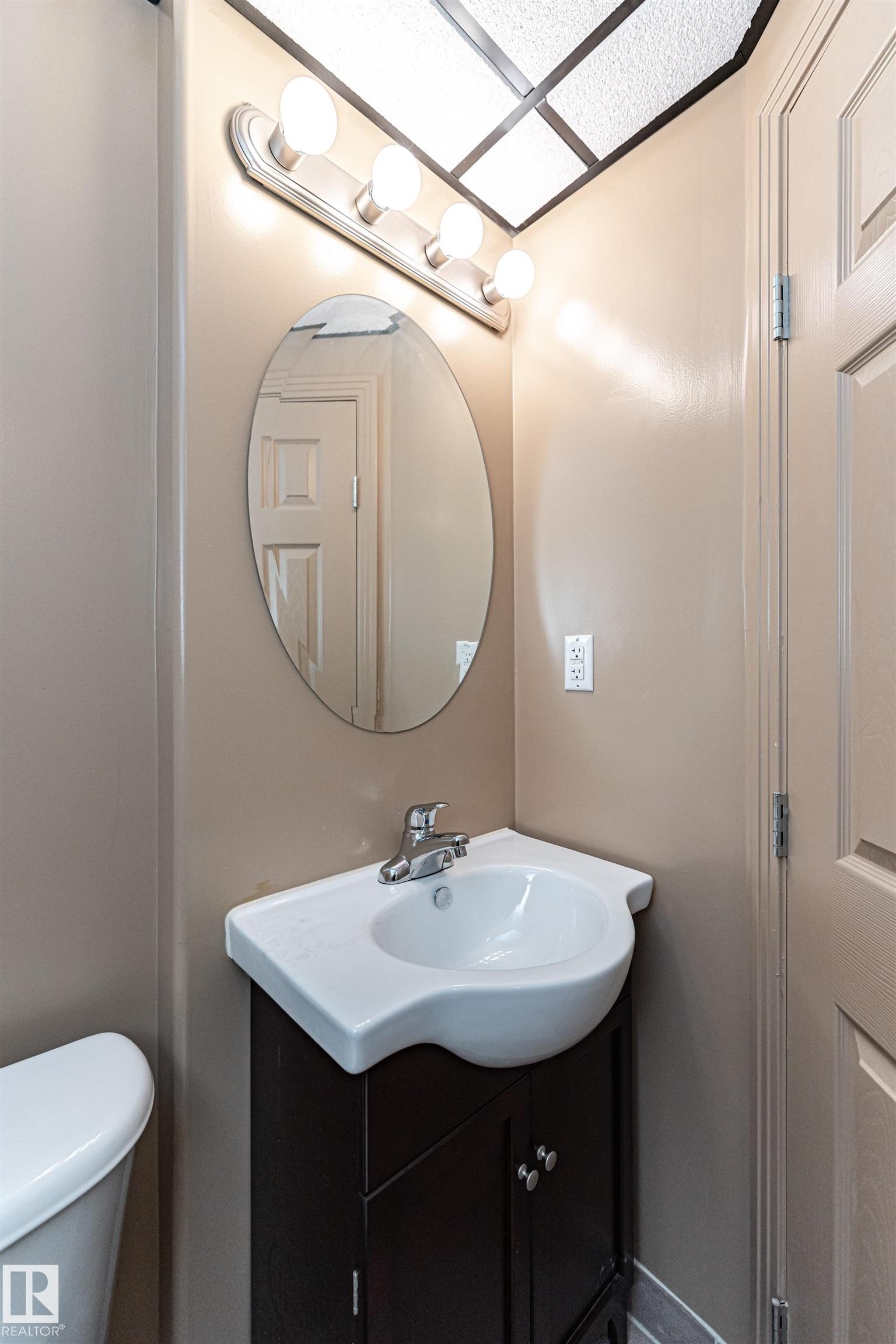 Vanity with integrated sink, dark wood-finish cabinetry, chrome faucet, and oval mirror - 12241 93 Street Nw, Edmonton, AB - Indoor Photo Showing Bathroom