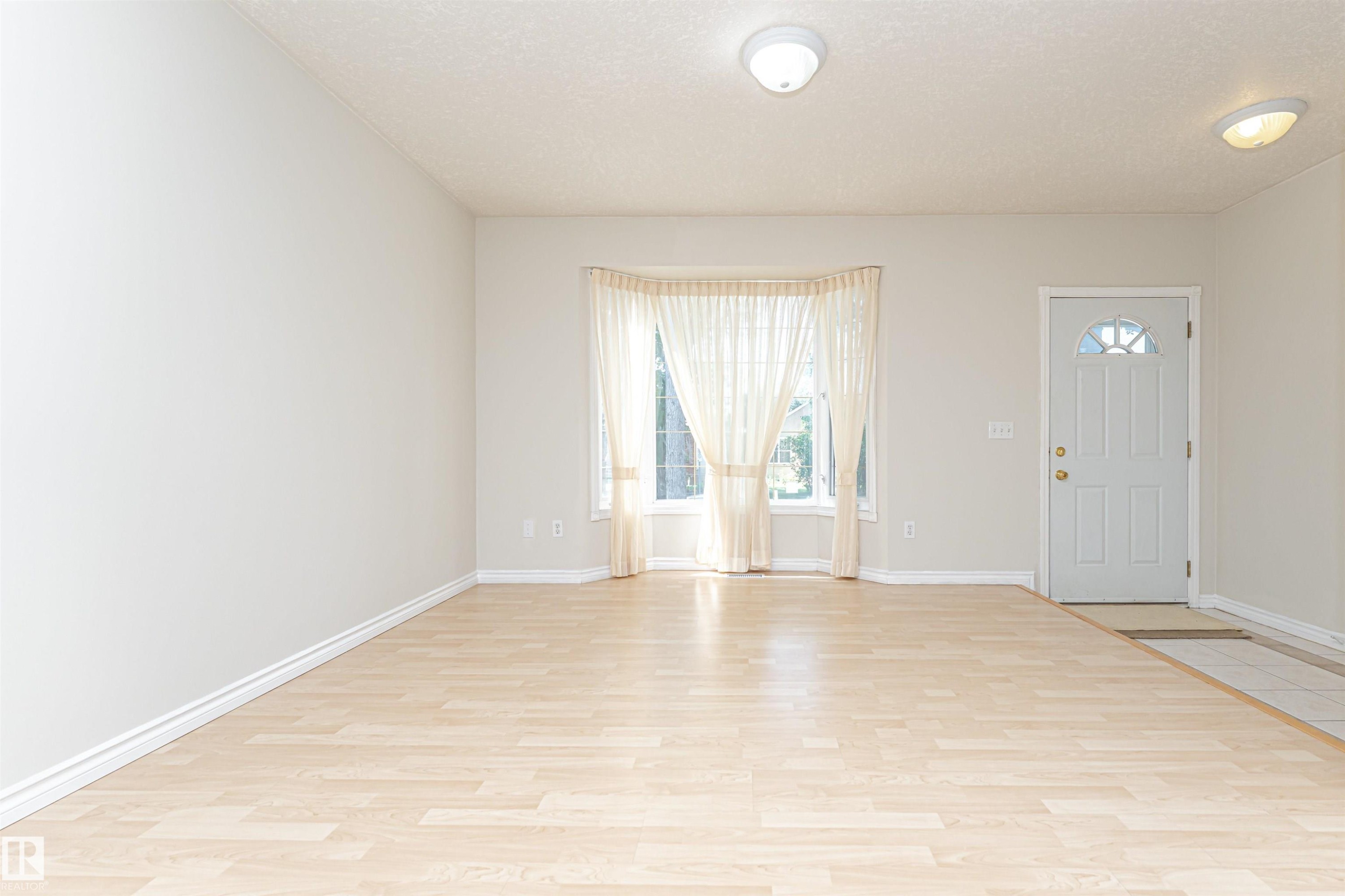 Light wood-finish flooring with a tile entry, a white front door featuring a decorative window, and a bay window - 12241 93 Street Nw, Edmonton, AB - Indoor Photo Showing Other Room