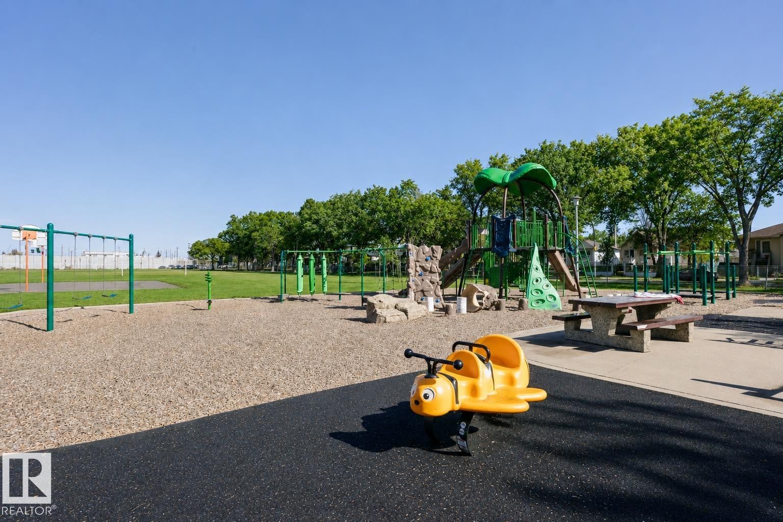 Recreational area featuring a playground structure with slides, swings, and climbing elements, alongside an open grassy field - 12241 93 Street Nw, Edmonton, AB - Outdoor