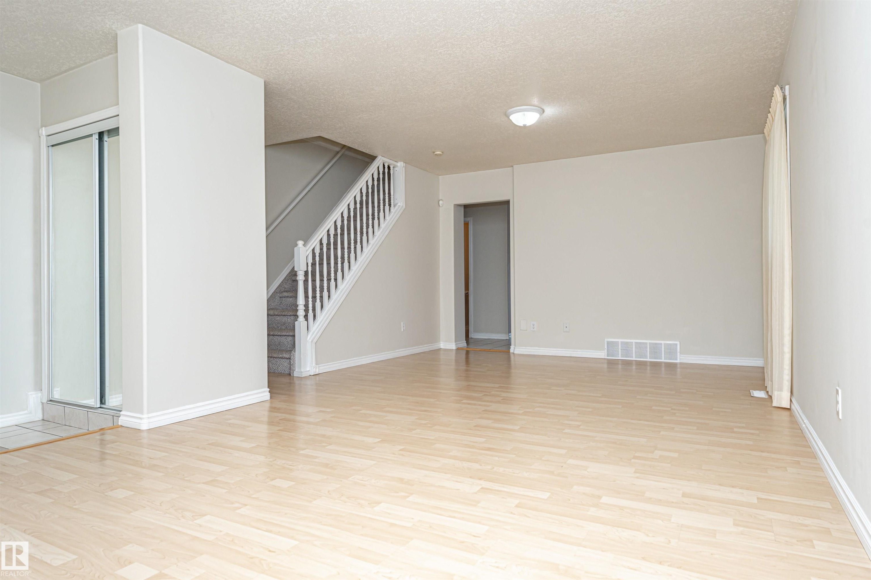 Light wood-finish flooring, staircase with carpeted treads and white banister, overhead flush mount lighting, sliding closet doors with frosted panels, and neutral wall tones - 12241 93 Street Nw, Edmonton, AB - Indoor Photo Showing Other Room