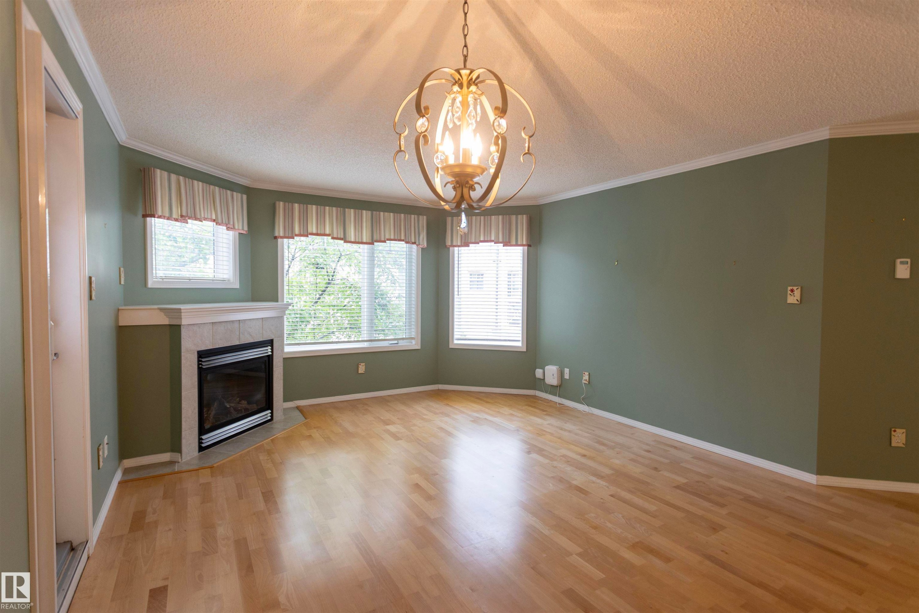 Recessed fireplace with tile surround, wood-finish flooring, multiple windows, and decorative ceiling fixture - #204 2420 108 St Nw, Edmonton, AB