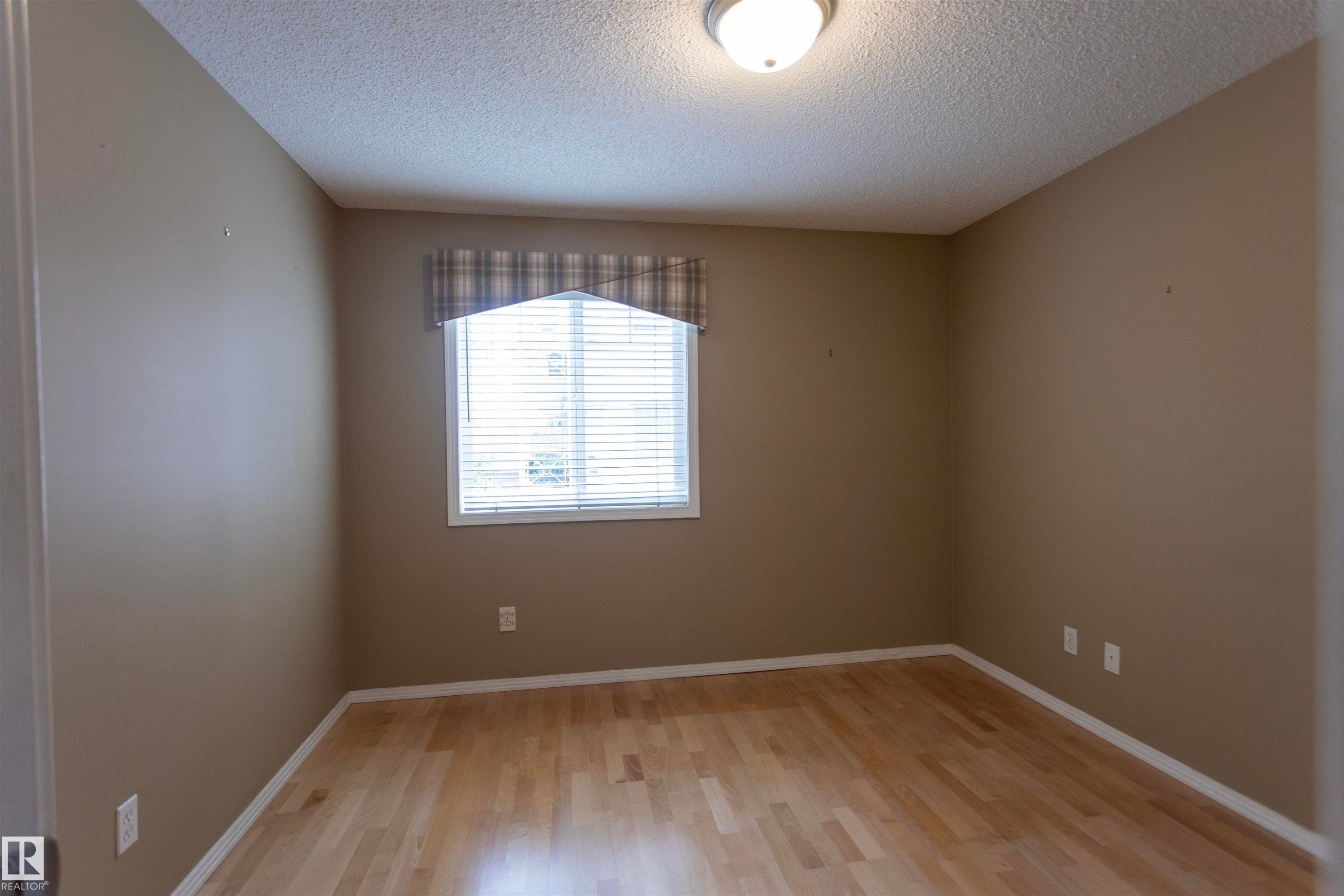 Warm neutral wall tones, wood-finish flooring, and a flush mount ceiling light - #204 2420 108 St Nw, Edmonton, AB