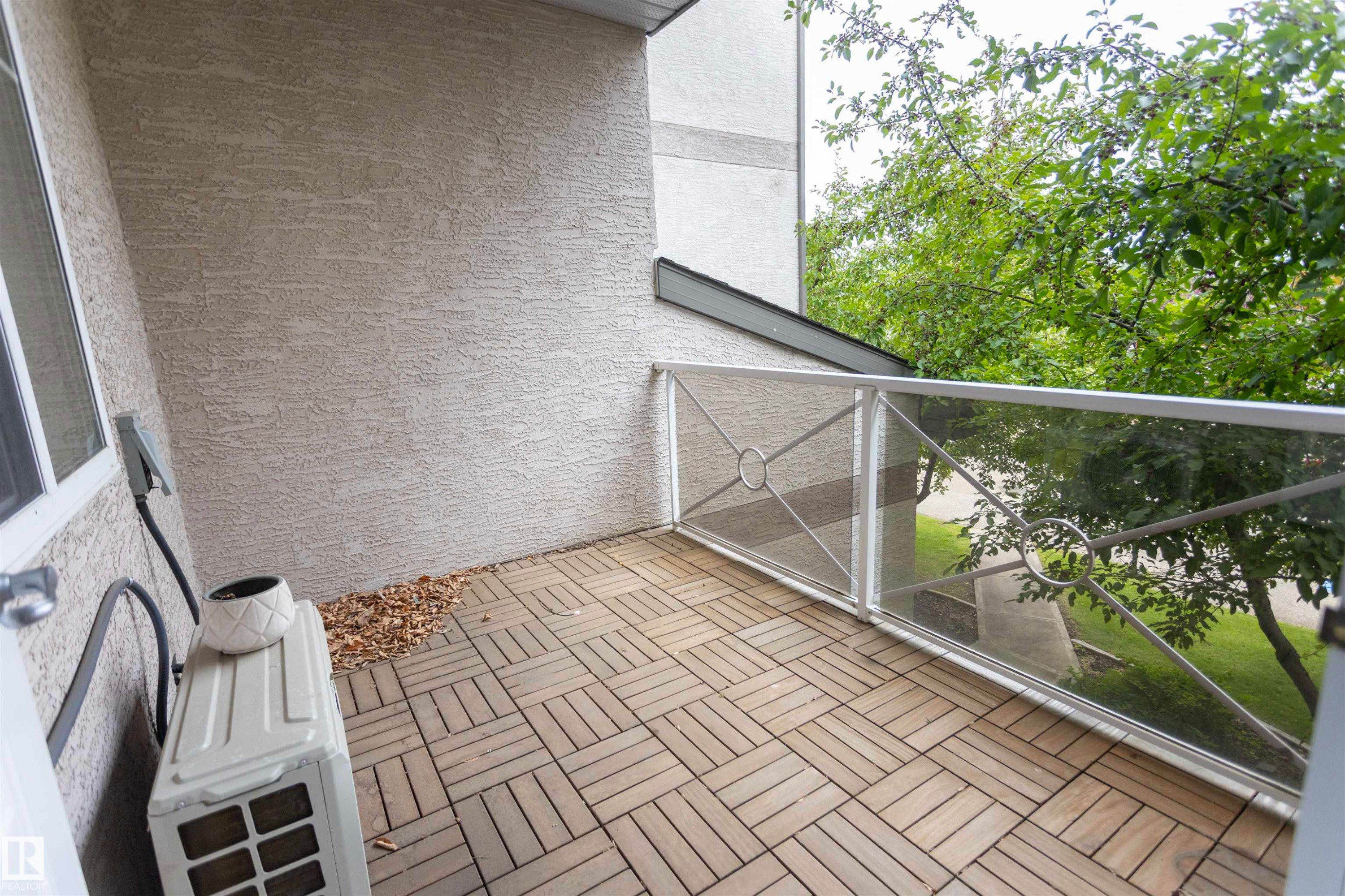 Private balcony with wood-finish tile flooring, stucco exterior walls, and a metal and glass railing - #204 2420 108 St Nw, Edmonton, AB