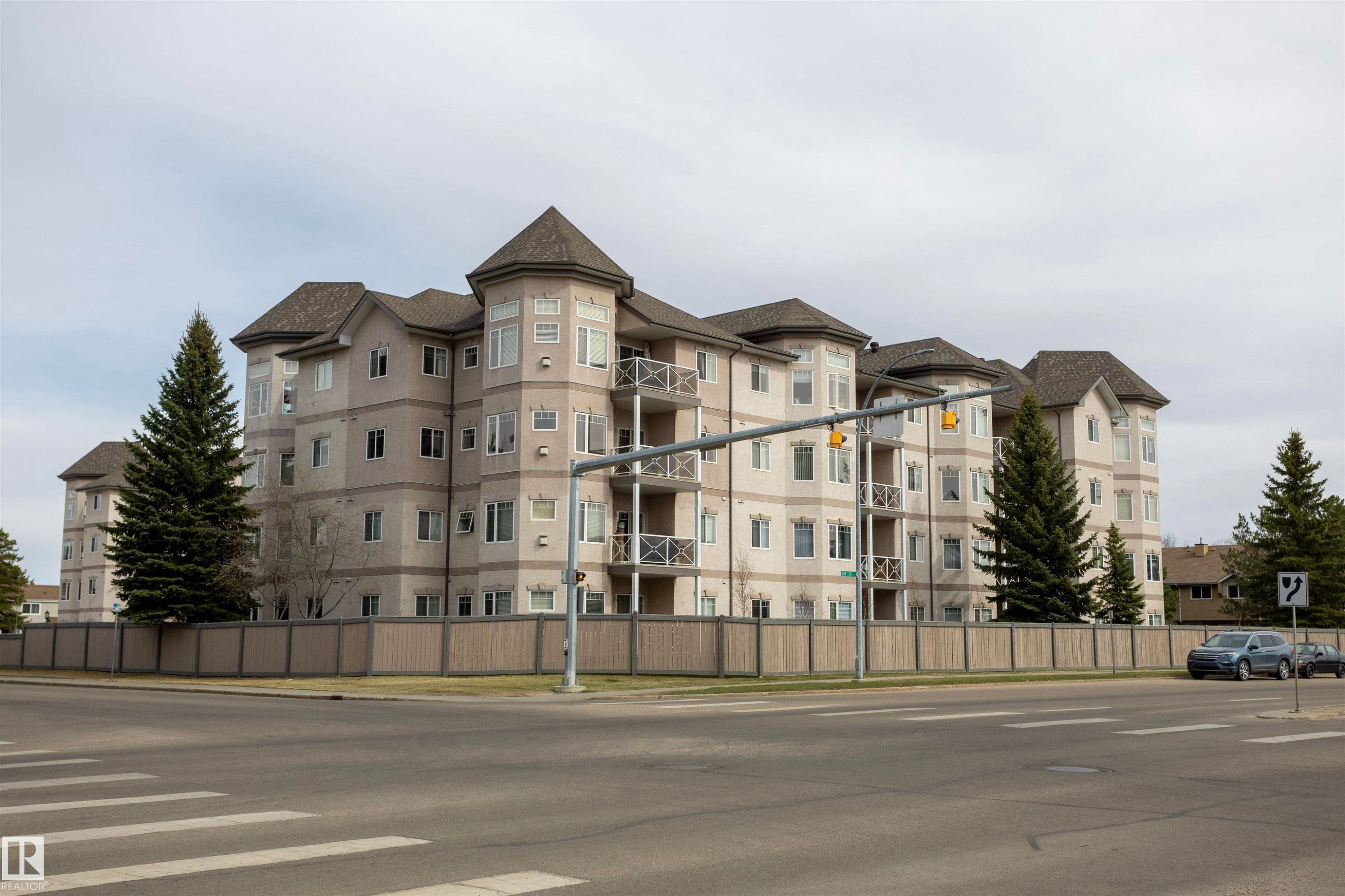 Multi-story building featuring turret-style architectural elements, private balconies, and a perimeter fence - #204 2420 108 St Nw, Edmonton, AB
