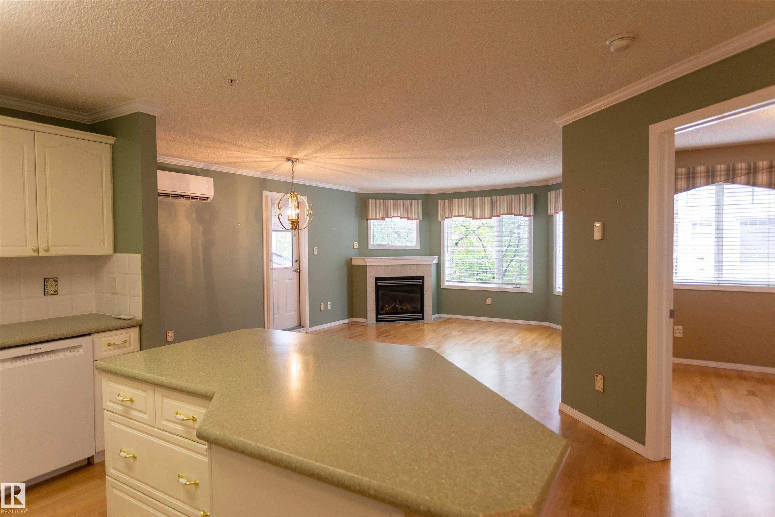 Kitchen island with integrated cabinetry and light-toned countertop, wood-finish flooring, and a fireplace with a mantel - #204 2420 108 St Nw, Edmonton, AB