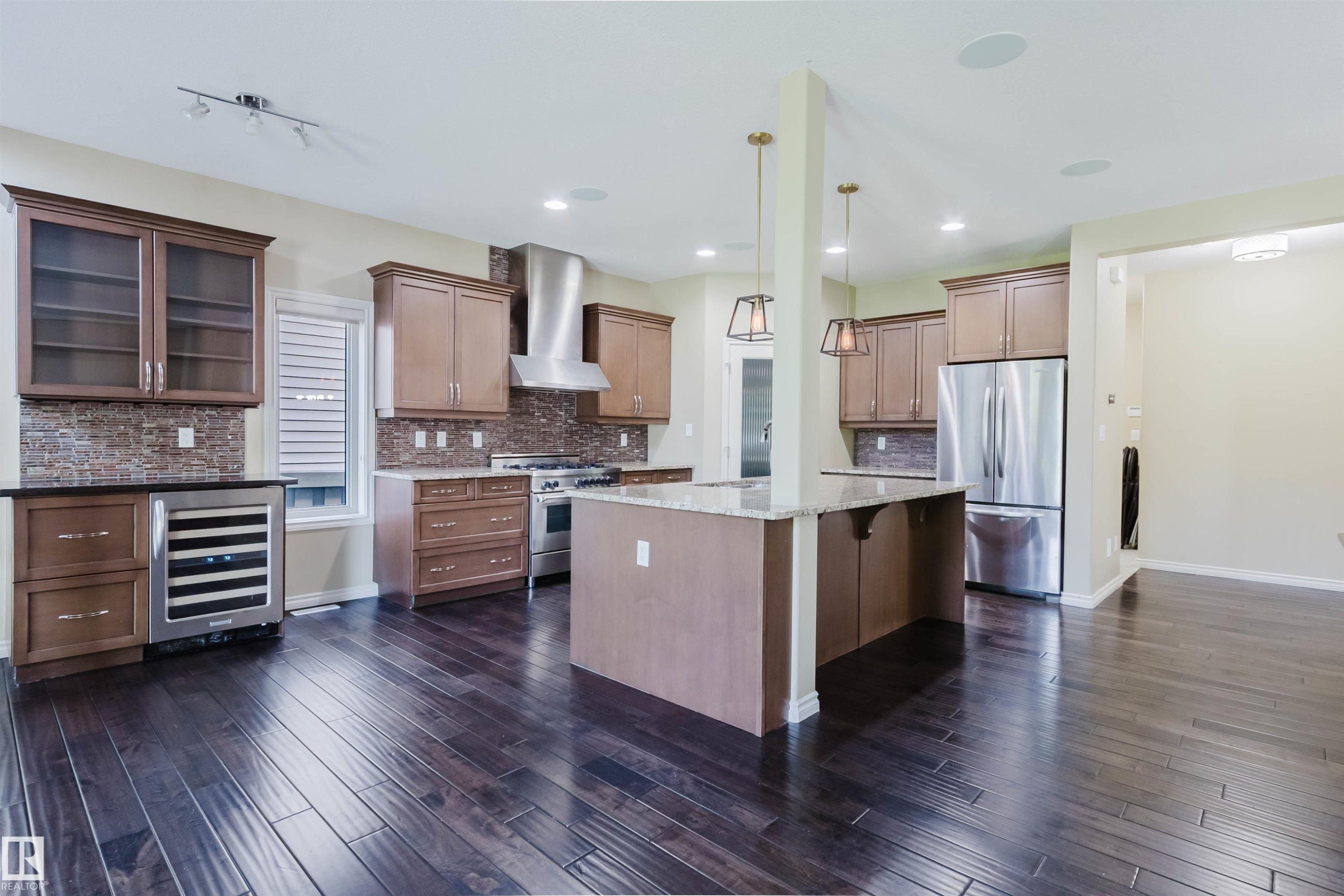 Kitchen featuring dark wood-finish flooring, a central island with a light-colored countertop, stainless steel appliances, and wood cabinetry with glass-front uppers - 864 Armitage Wynd Sw, Edmonton, AB - Indoor Photo Showing Kitchen With Upgraded Kitchen