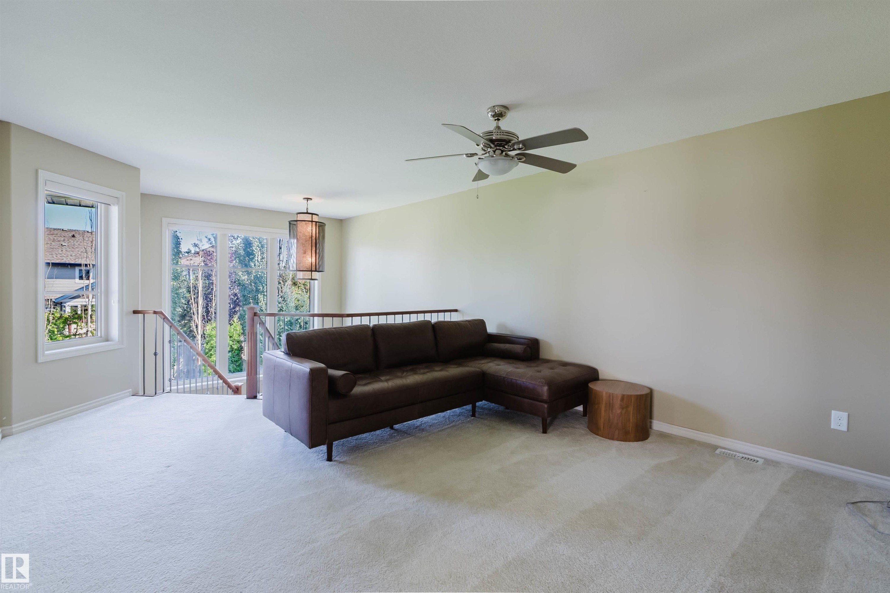 Spacious carpeted area with abundant natural light, featuring a ceiling fan and a modern decorative pendant light - 864 Armitage Wynd Sw, Edmonton, AB - Indoor Photo Showing Other Room