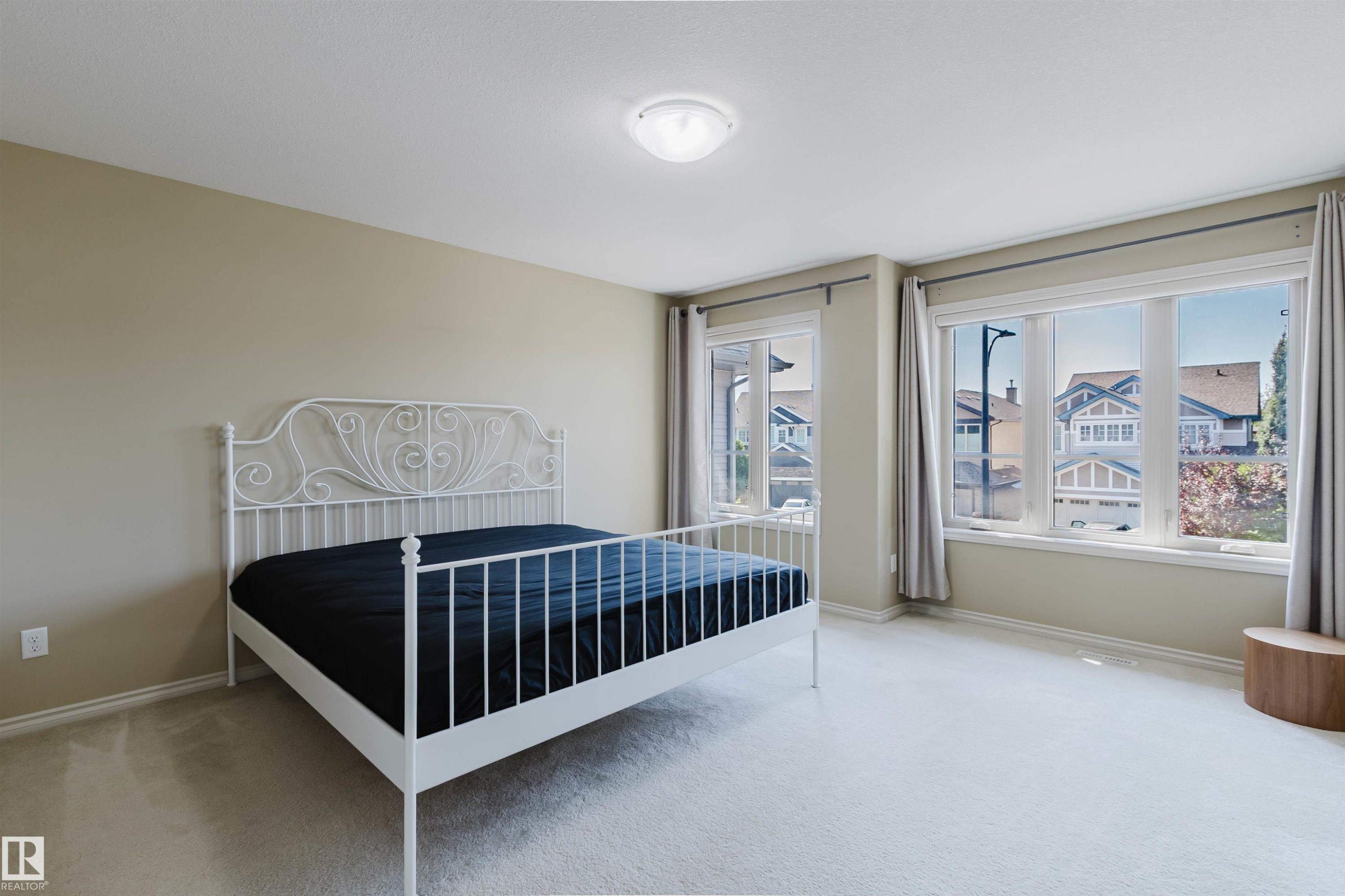 Neutral painted walls, light-colored carpeting, large windows with curtain rods, and a ceiling-mounted light fixture - 864 Armitage Wynd Sw, Edmonton, AB - Indoor Photo Showing Bedroom