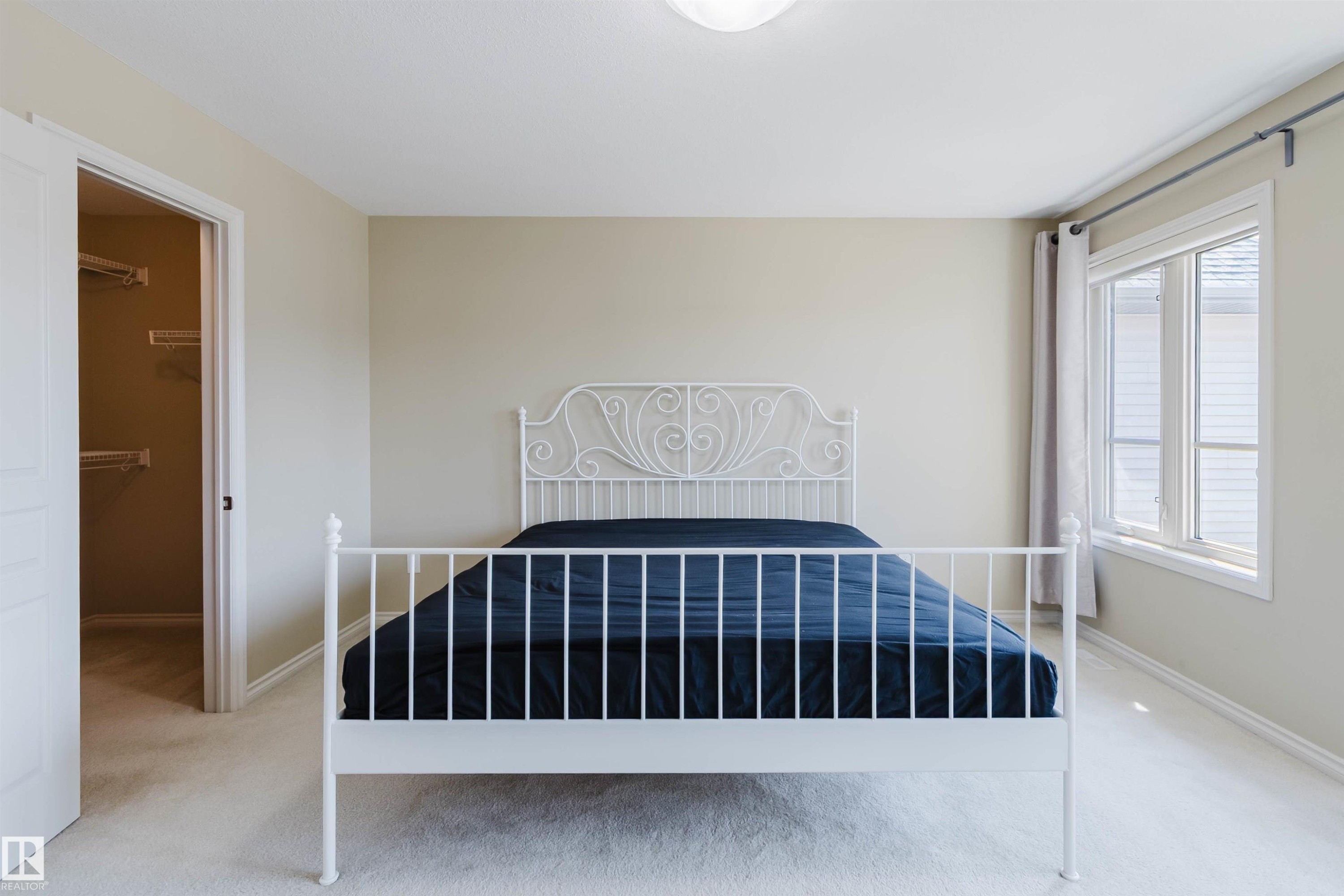 Wall-to-wall carpeting, walk-in closet with built-in shelving, and a large window with privacy blinds - 864 Armitage Wynd Sw, Edmonton, AB - Indoor Photo Showing Bedroom