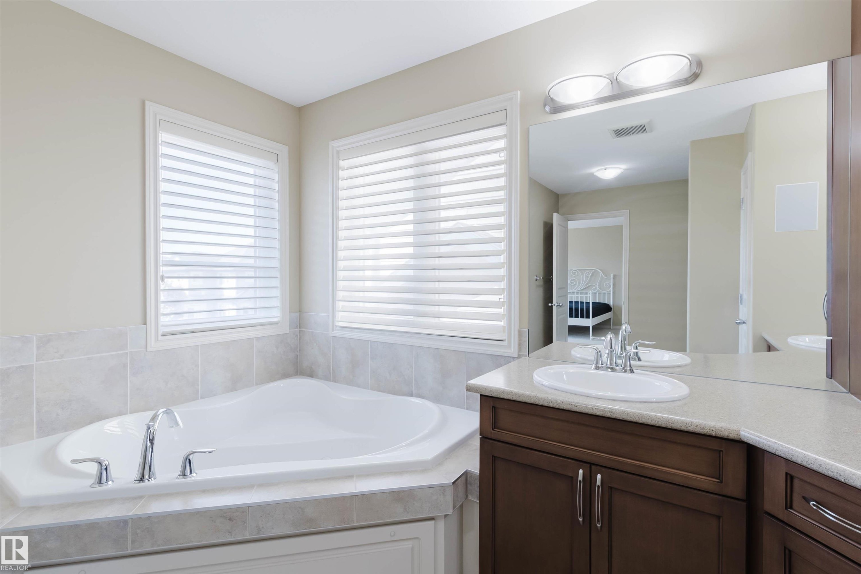 Corner soaking tub with chrome fixtures, dual windows with blinds, wood-finish vanity with countertop, and dual sinks - 864 Armitage Wynd Sw, Edmonton, AB - Indoor Photo Showing Bathroom
