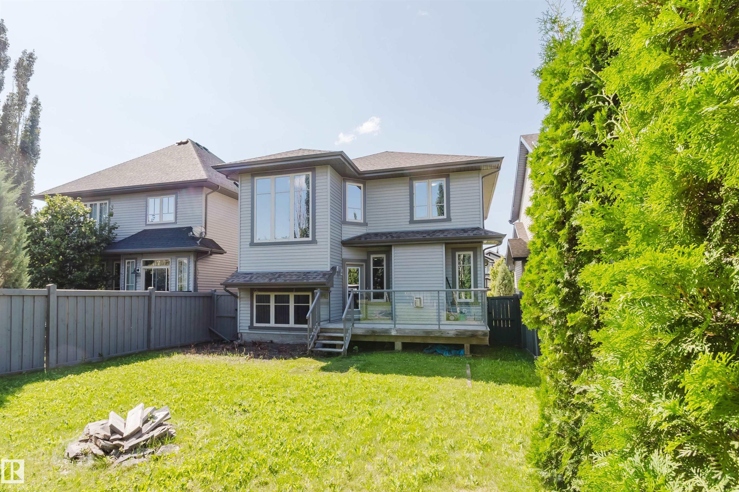 Expansive backyard with a manicured lawn, multi-level deck featuring glass railings, and upper-level bay windows - 864 Armitage Wynd Sw, Edmonton, AB - Outdoor