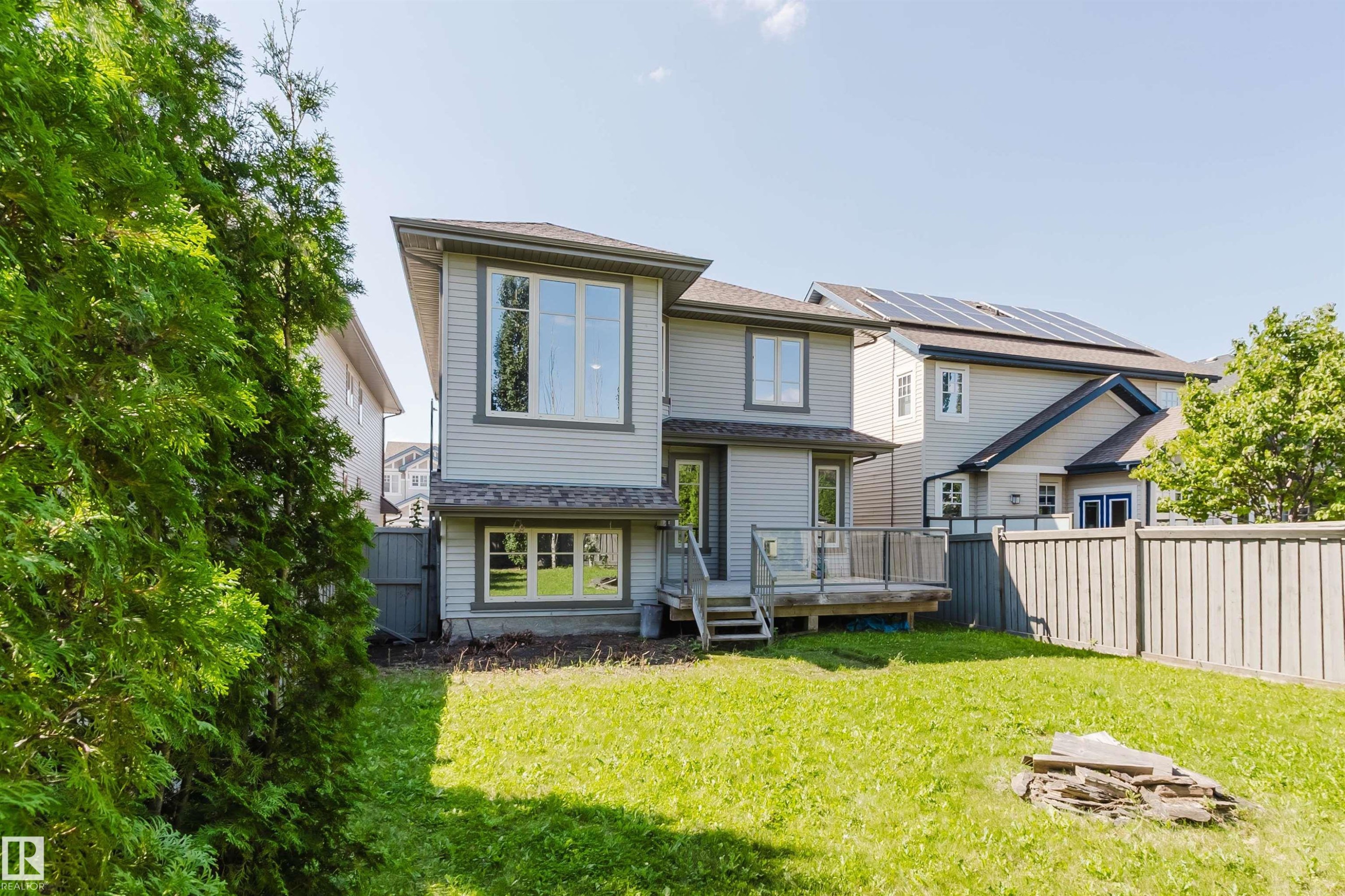 Expansive backyard featuring a manicured lawn, a wooden deck with glass railing, and a privacy fence - 864 Armitage Wynd Sw, Edmonton, AB - Outdoor