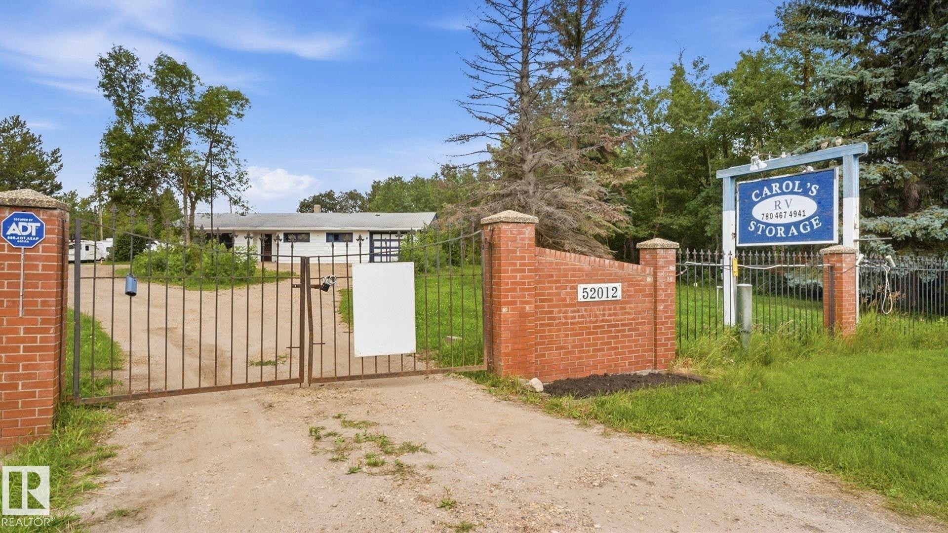 Gated entry with brick pillars, a long driveway, and a white single-story structure with a dark roof - 52012 Hwy 21, Rural Strathcona County, AB - Outdoor