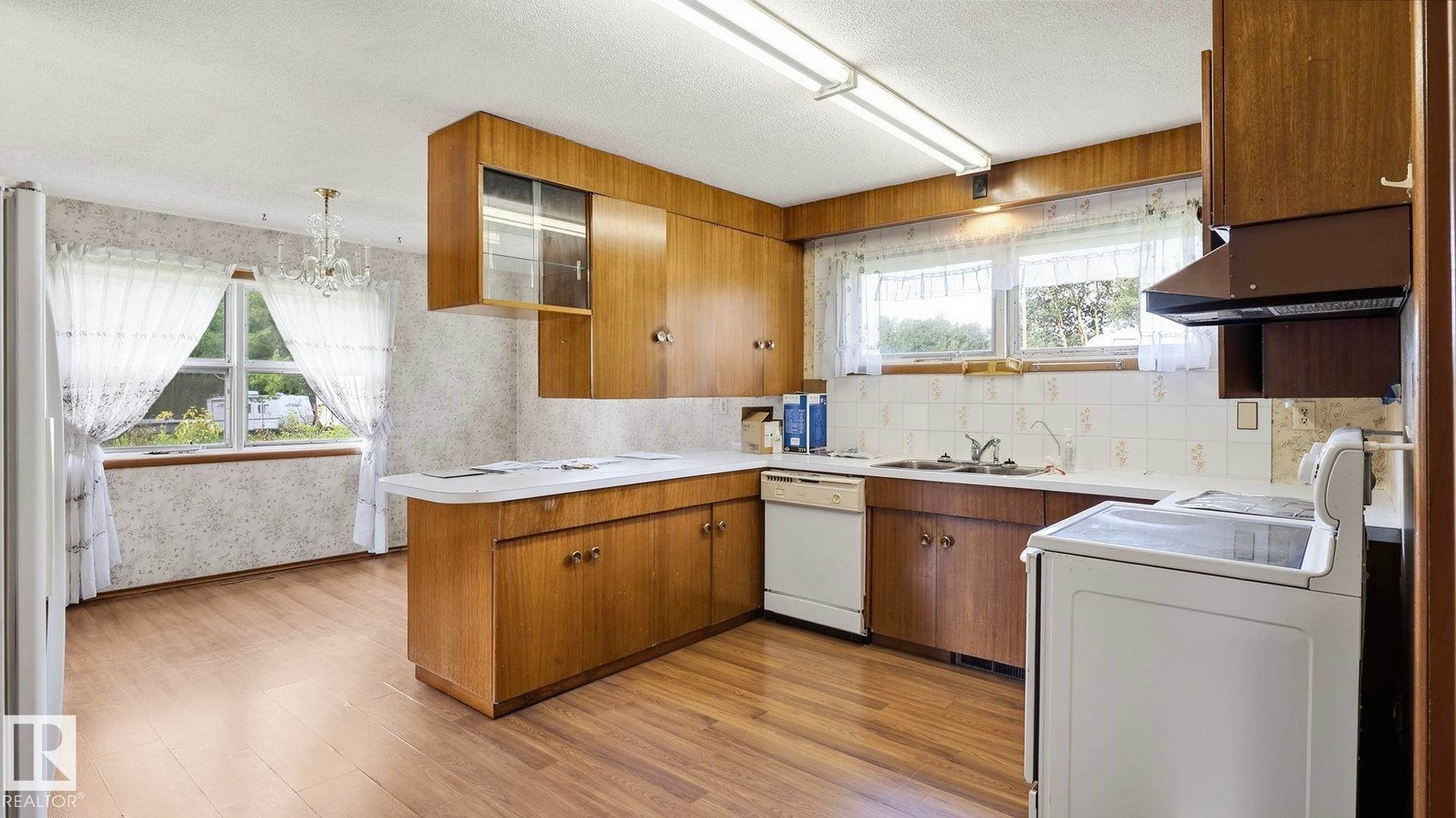 Kitchen featuring wood-finish flooring, wood cabinetry with glass-front accents, and a white tile backsplash - 52012 Hwy 21, Rural Strathcona County, AB - Indoor Photo Showing Kitchen With Double Sink