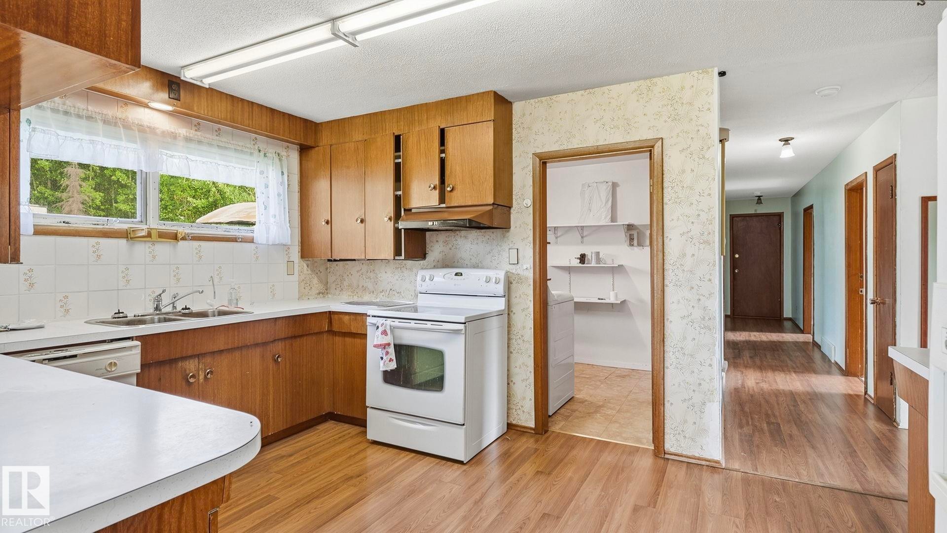 Kitchen featuring wood-finish cabinetry, white countertops, a tile backsplash, and wood-finish flooring - 52012 Hwy 21, Rural Strathcona County, AB - Indoor Photo Showing Kitchen With Double Sink