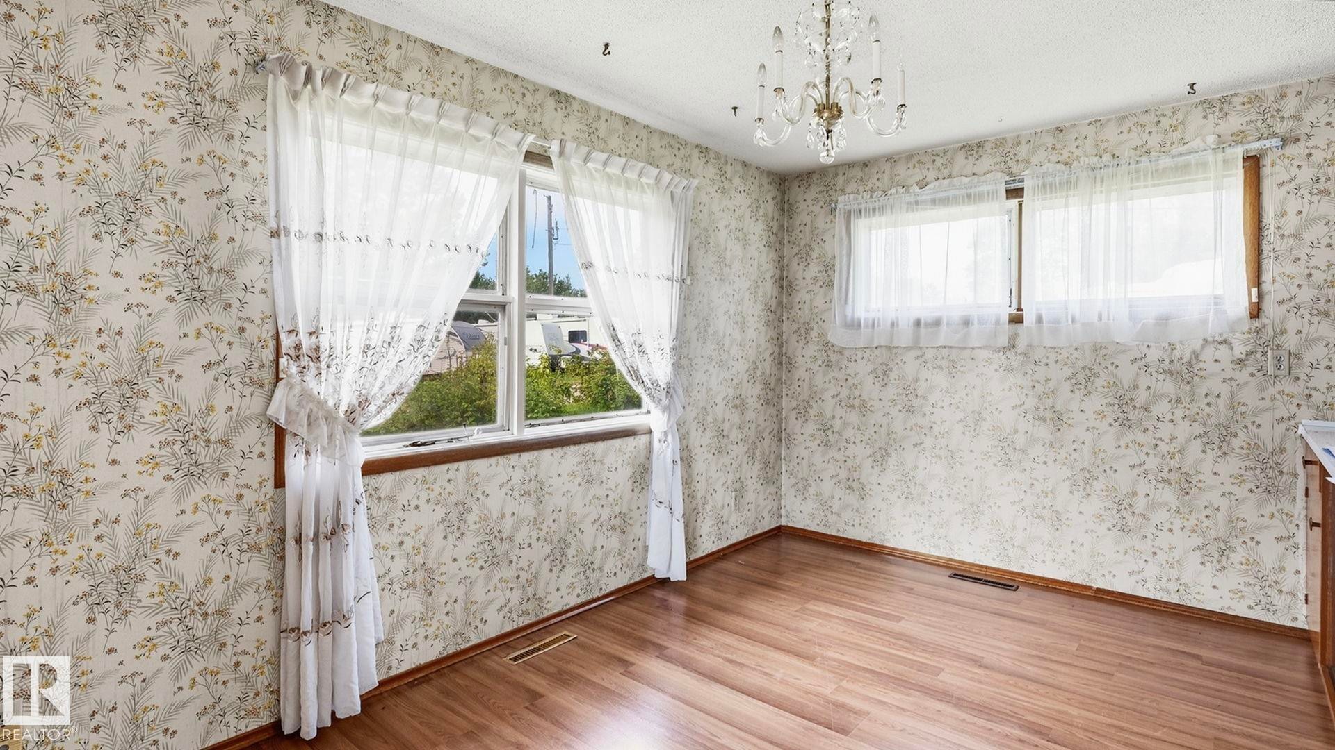 Wood-finish flooring with floral pattern wallpaper, a crystal chandelier, and multiple windows - 52012 Hwy 21, Rural Strathcona County, AB - Indoor Photo Showing Other Room