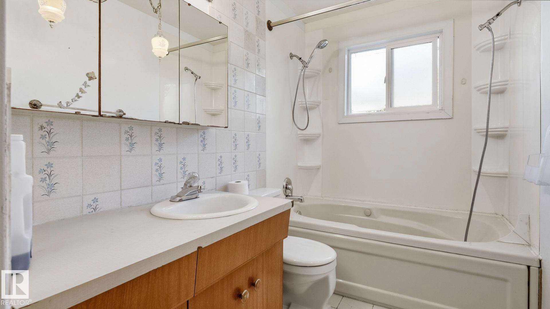 Bathroom featuring a built-in bathtub, a window, a vanity with an integrated sink, and patterned wall tiles - 52012 Hwy 21, Rural Strathcona County, AB - Indoor Photo Showing Bathroom