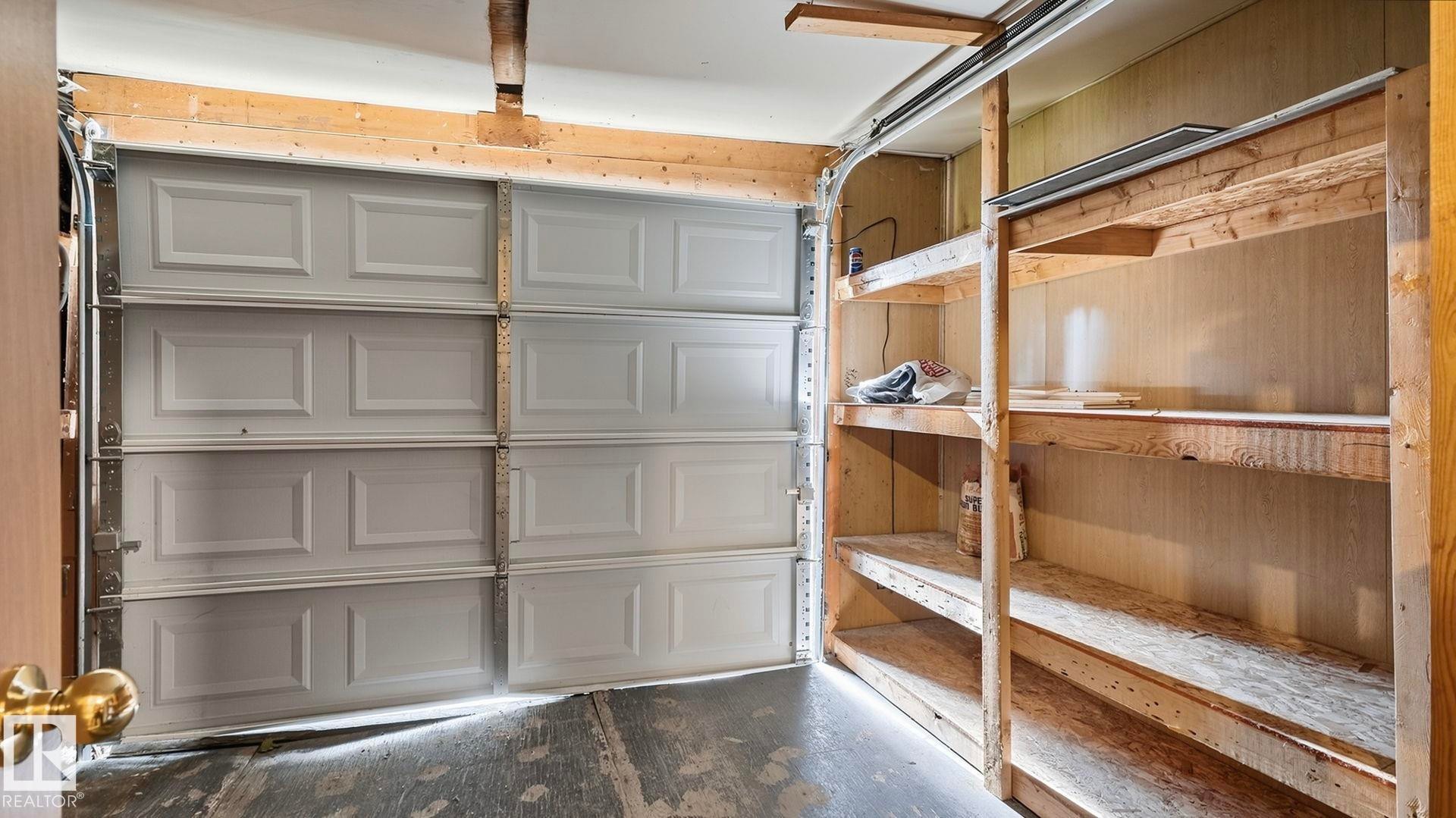 Attached garage with a paneled overhead door, concrete flooring, and built-in wood shelving - 52012 Hwy 21, Rural Strathcona County, AB - Indoor