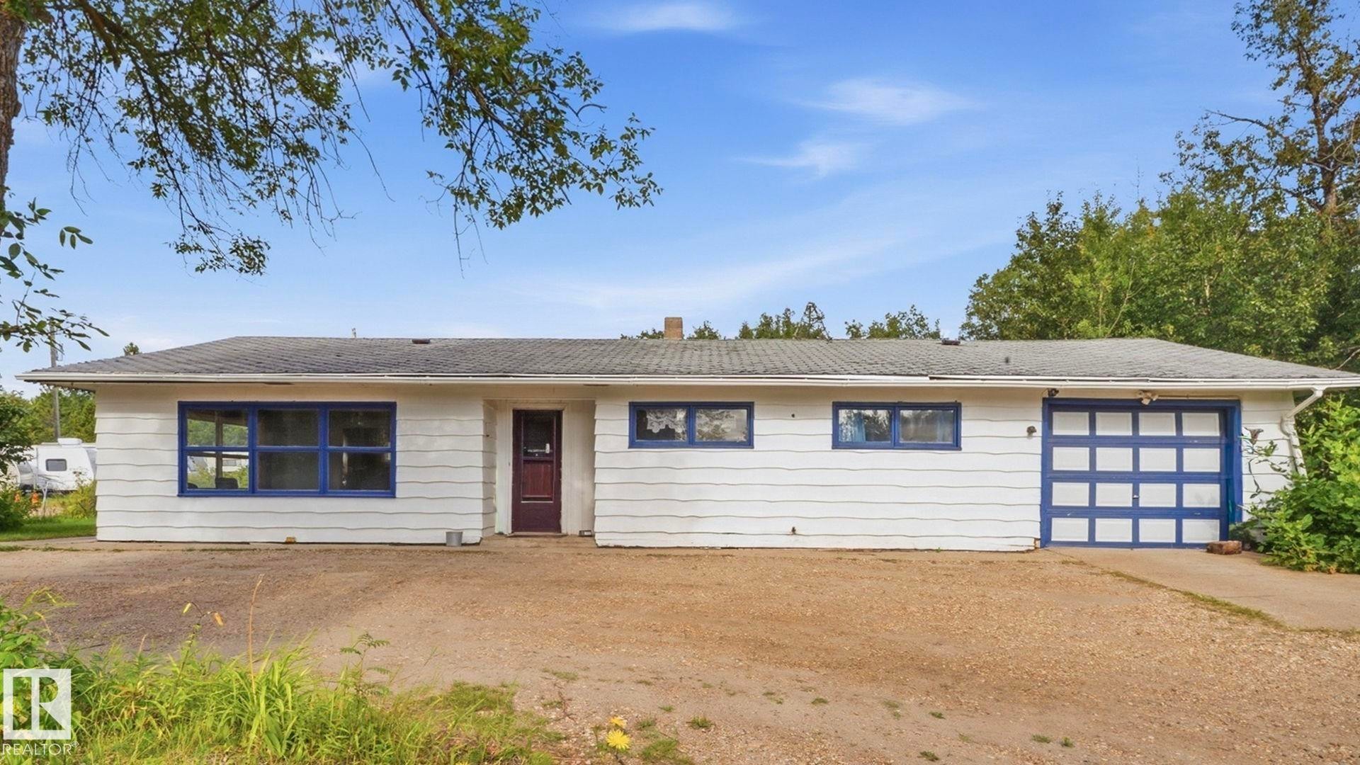 Ranch-style residence featuring white siding, a dark roof, blue window frames, and an integrated garage with a blue sectional door - 52012 Hwy 21, Rural Strathcona County, AB - Outdoor