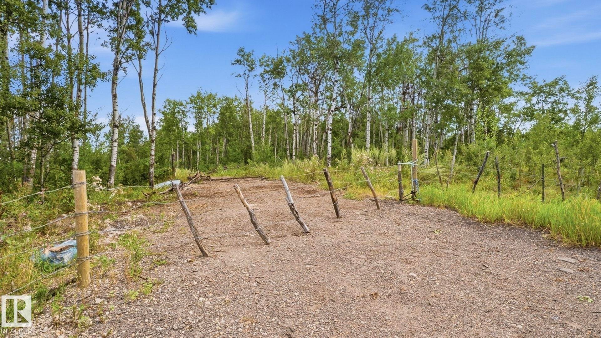 Gravel area with a partial barbed wire fence and natural wood posts, bordered by varied foliage and mature trees - 52012 Hwy 21, Rural Strathcona County, AB - Outdoor
