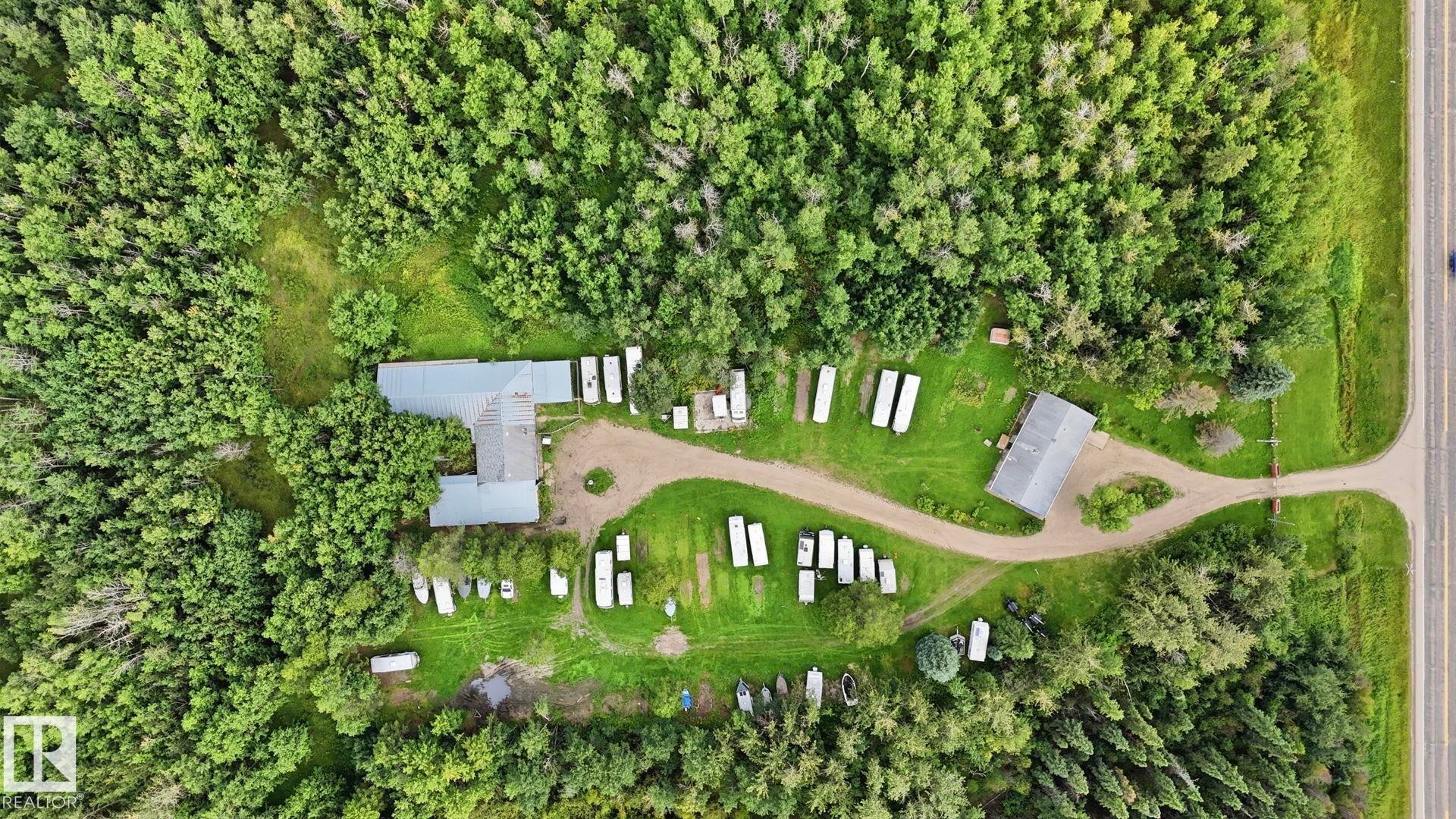 Extensive tree coverage surrounding the property, multiple structures with light-colored roofing, and a defined gravel driveway system - 52012 Hwy 21, Rural Strathcona County, AB - Outdoor